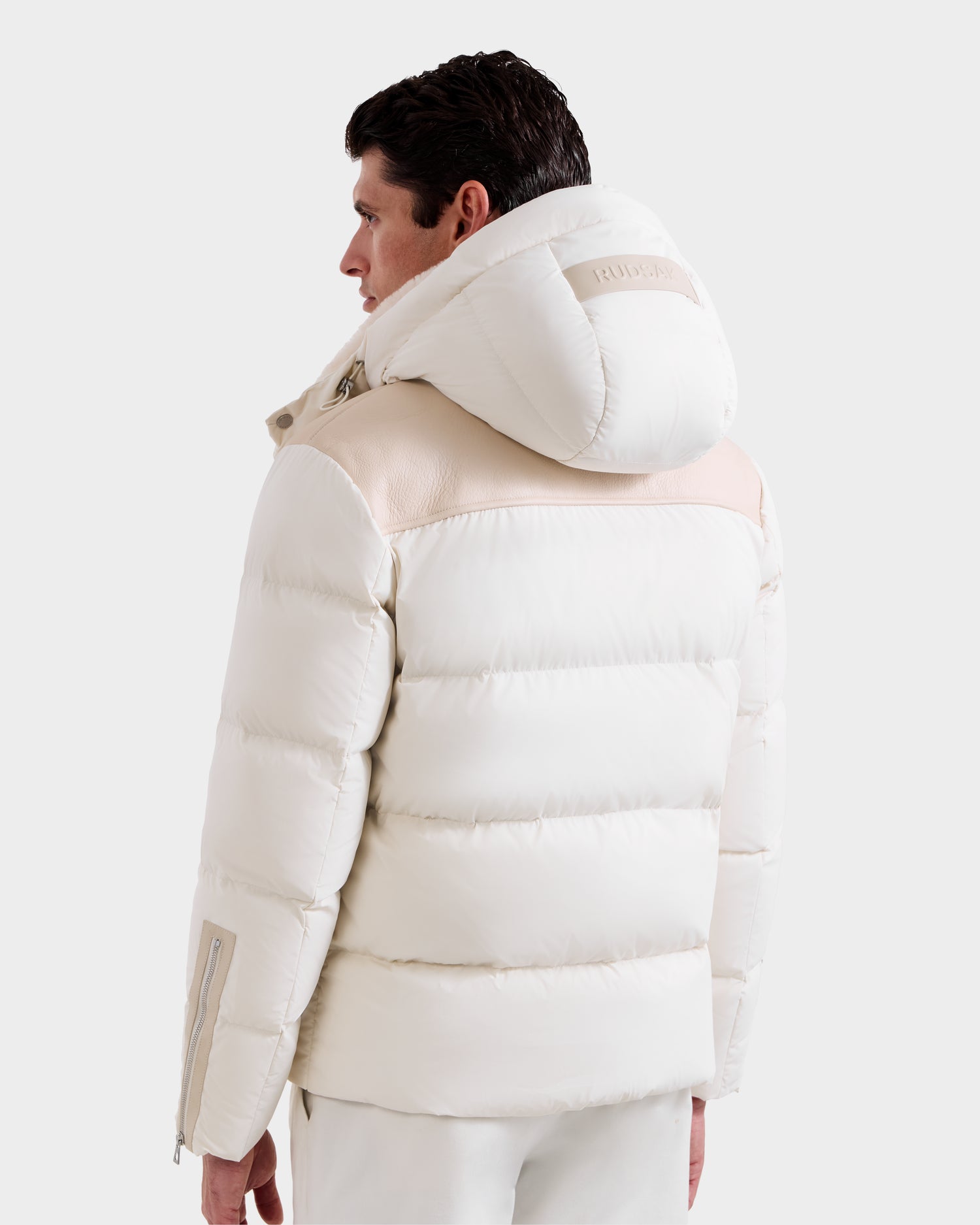 A person with short brown hair is seen from behind wearing the Rudsak SIMON - 6125597 Vanilla men’s quilted down puffer jacket with a large hood and light beige accents, standing against a plain white background.
