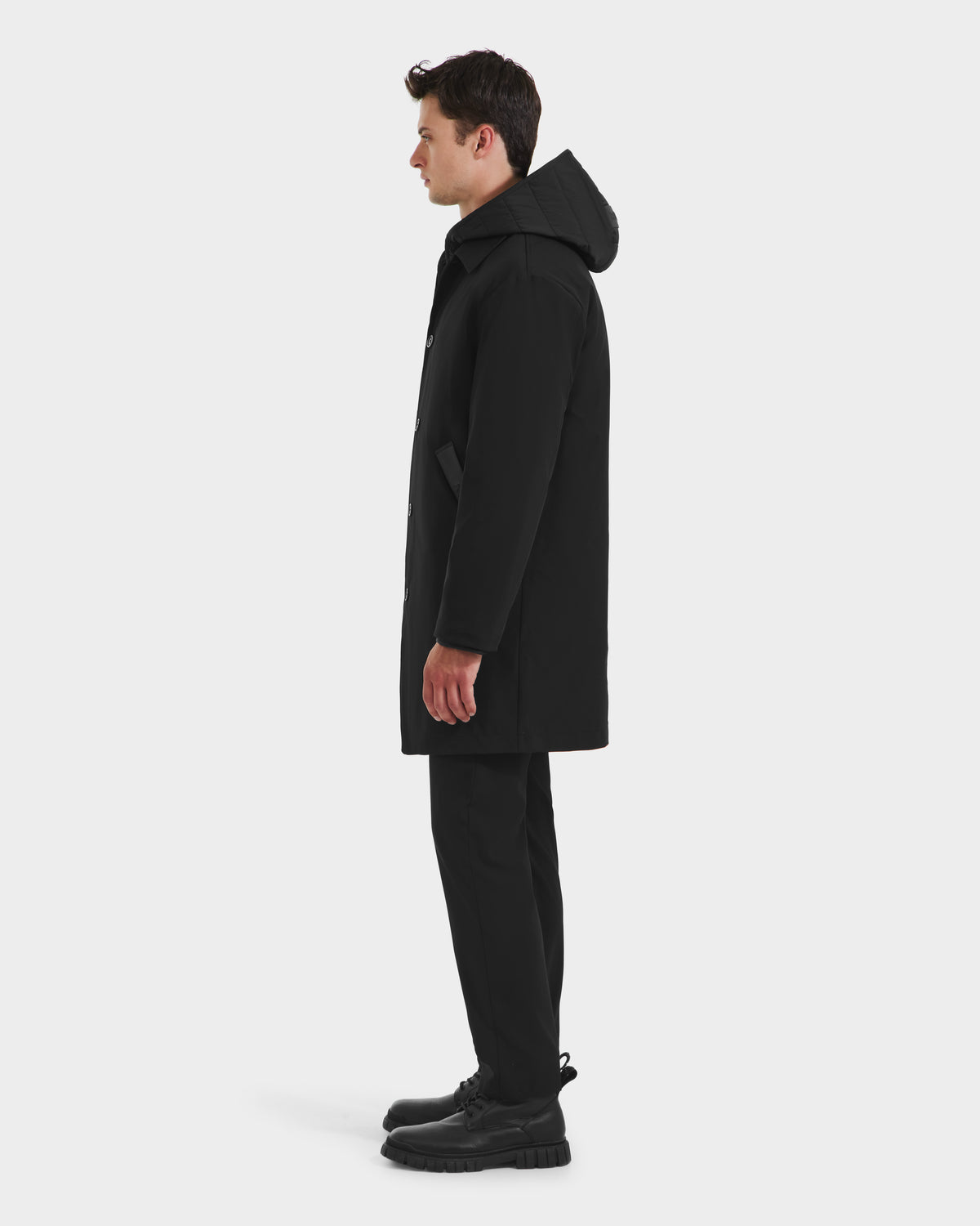 A man stands in profile wearing the Rudsak STANTON - 6125531 Black mens 3-in-1 overcoat, paired with black pants and shoes, against a plain white background.