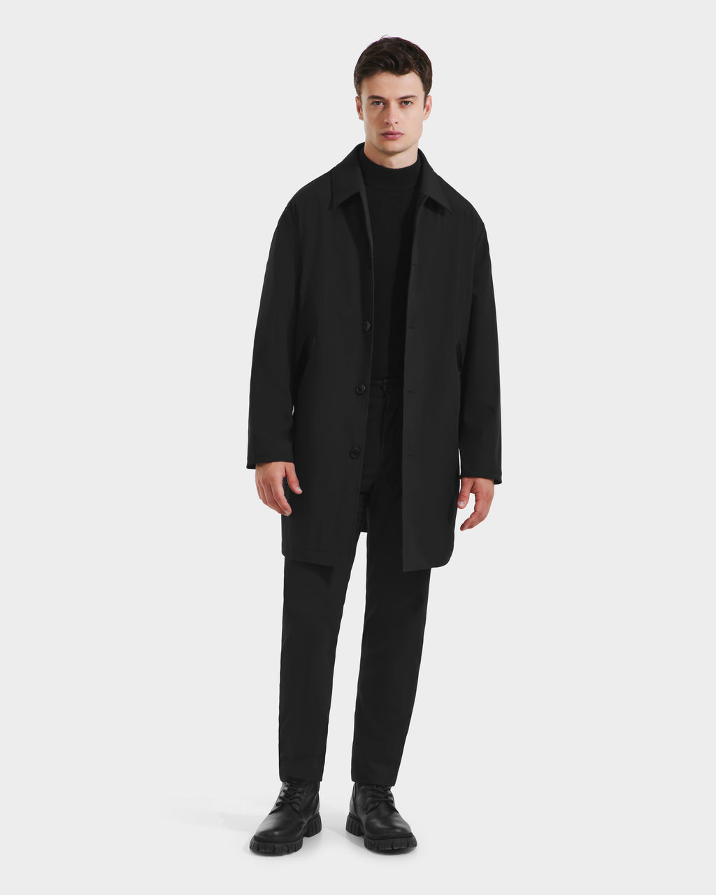 A person stands against a plain white background, wearing an all-black outfit featuring the Rudsak STANTON - 6125531 Black men’s weather-resistant 3-in-1 overcoat, paired with black pants, turtleneck sweater, and shoes.