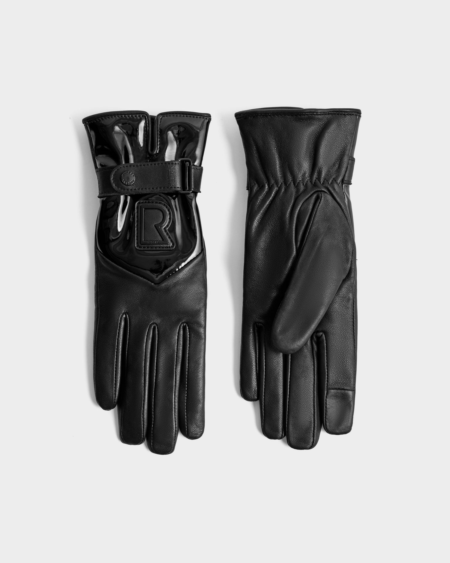 The Rudsak STROMBOLI - 8424509 Black women's leather gloves are shown with one palm and one back view, featuring a glossy strap and raised R emblem. These sleek, fitted winter gloves are displayed on a plain light background.