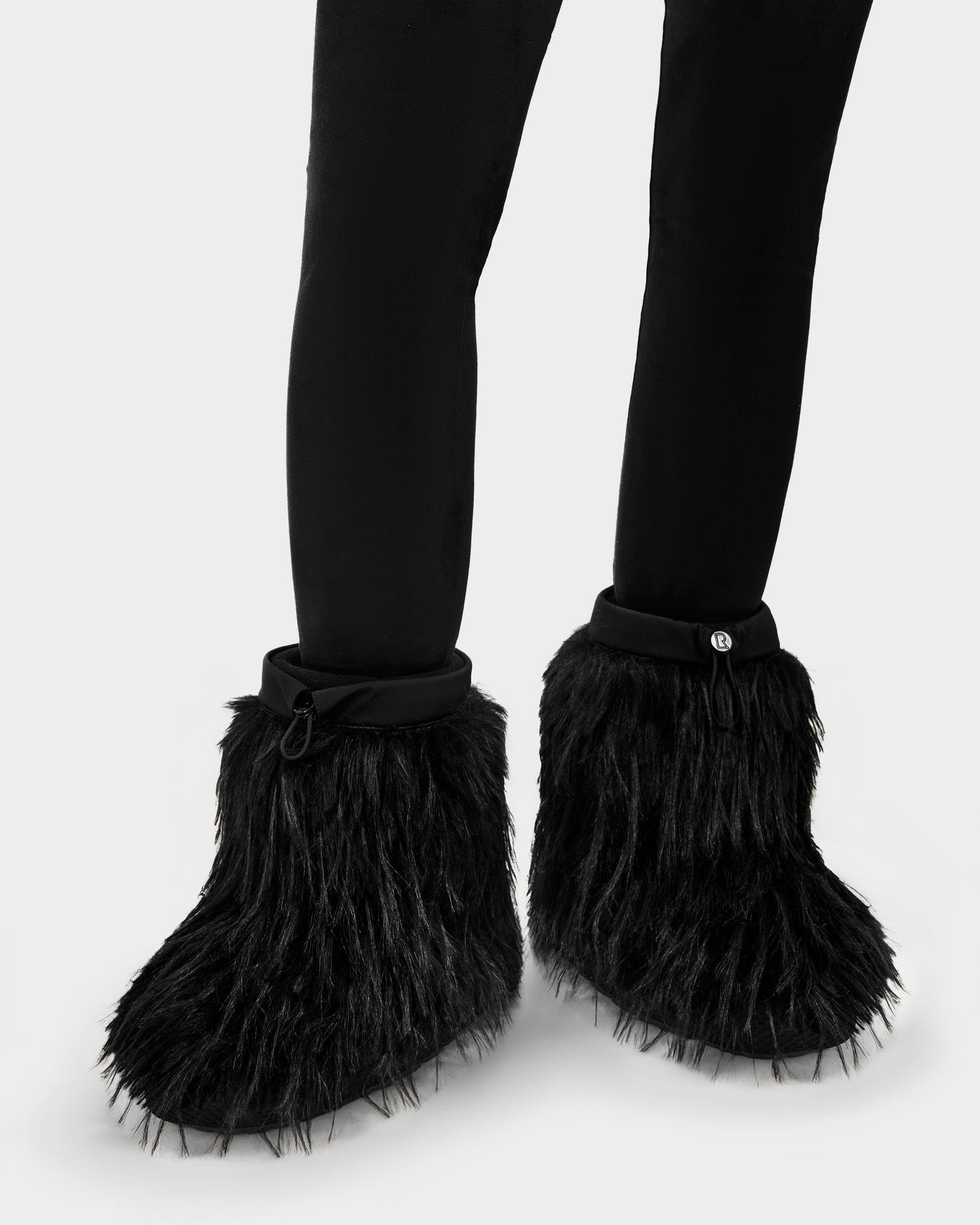 Someone stands against a plain white background wearing Rudsak's SUZIE G - 8225545 Black pants and fuzzy black monster slippers with claws, evoking a playful winter style.