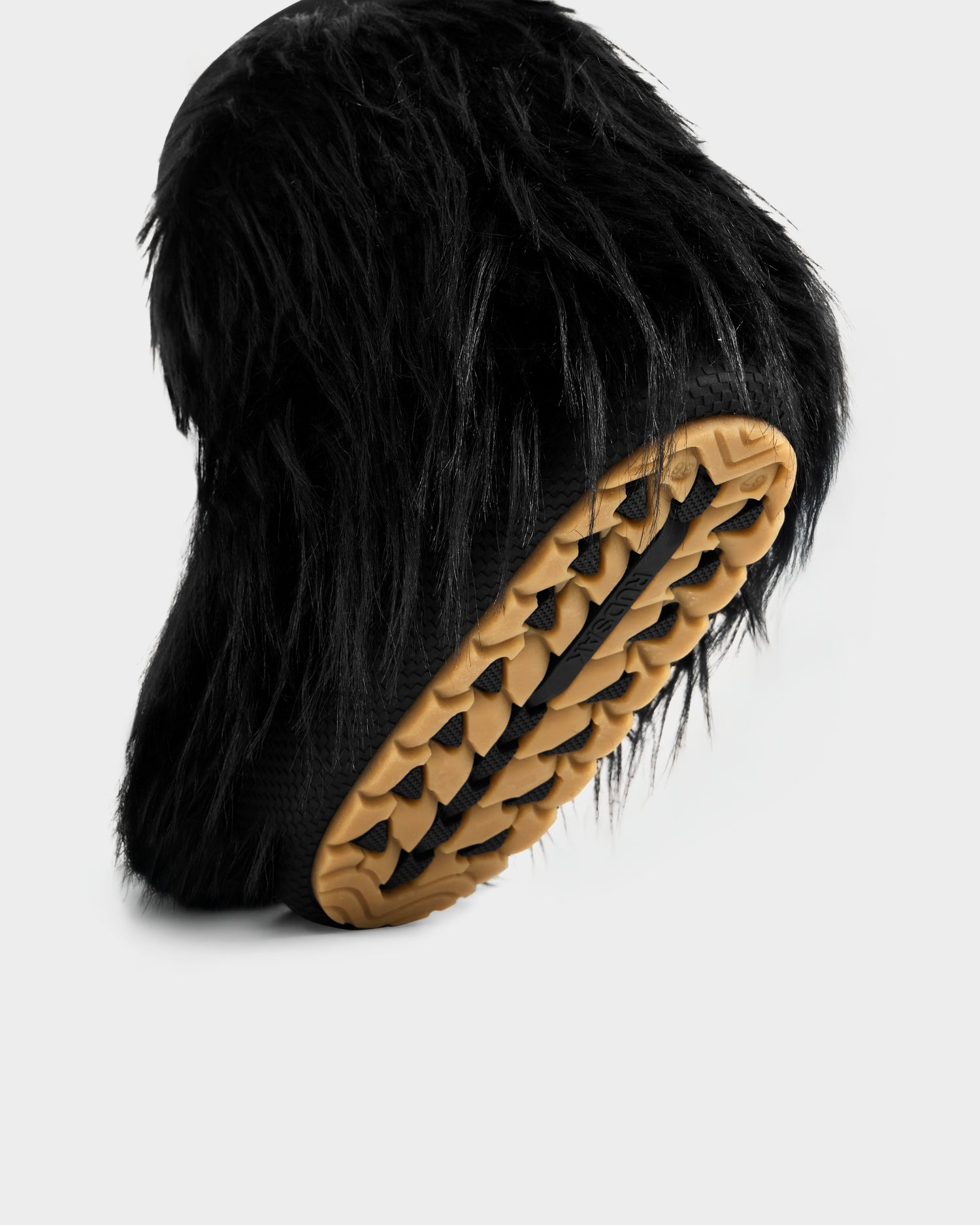 The SUZIE G - 8225545 Black by Rudsak is a women's black faux fur moon boot featuring long, shaggy fur and a tan textured rubber sole, shown against a plain white background.