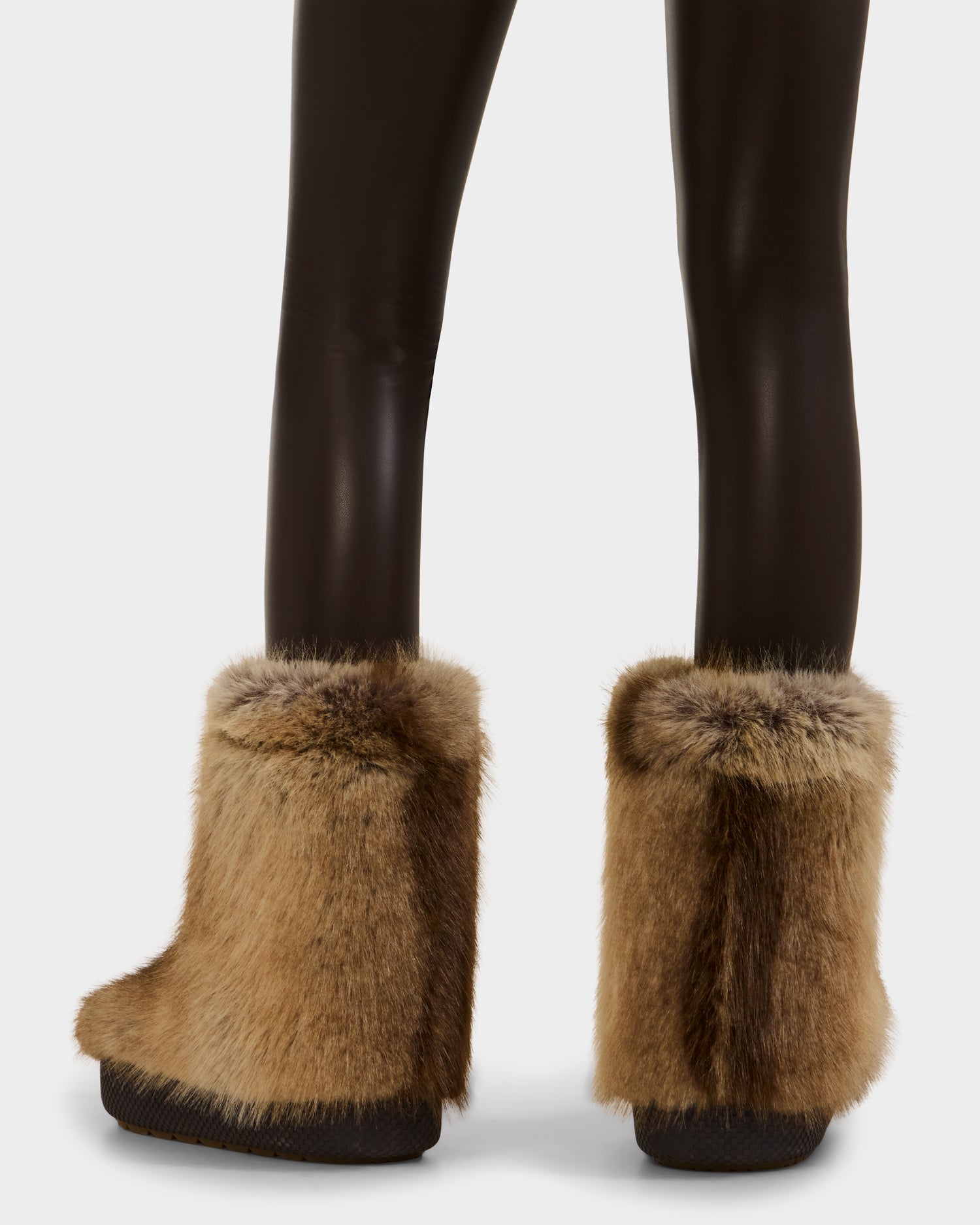 A person is shown from the back, wearing black leggings and Rudsak SUZIE - 8225052 Mix Mocha women’s faux fur moon boots against a plain background.