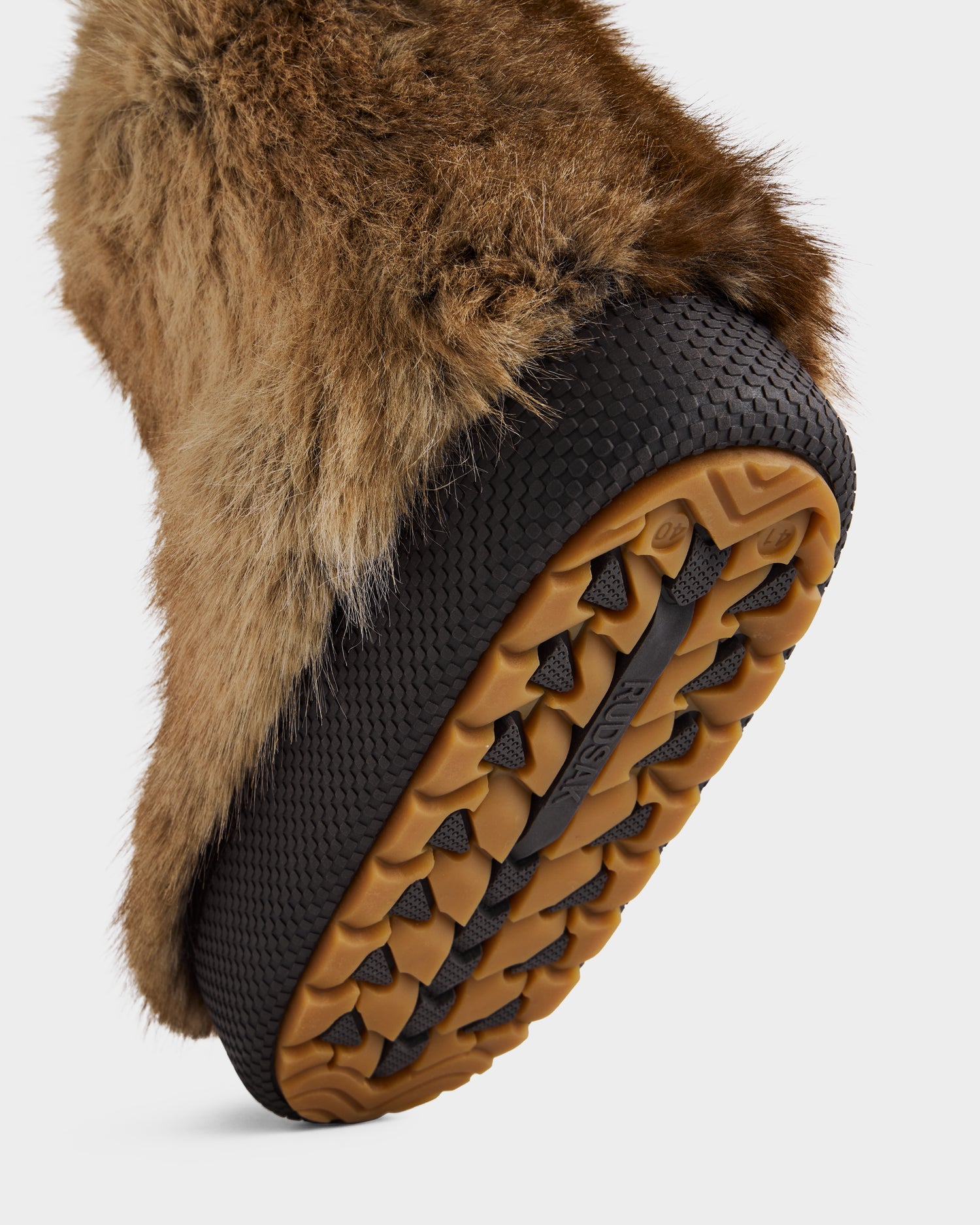 A close-up of the sole of the Rudsak SUZIE - 8225052 Mix Mocha women’s faux fur moon boot shows its rugged brown and black tread, thick mocha fur upper, and lifted profile that highlights its intricate winter style.