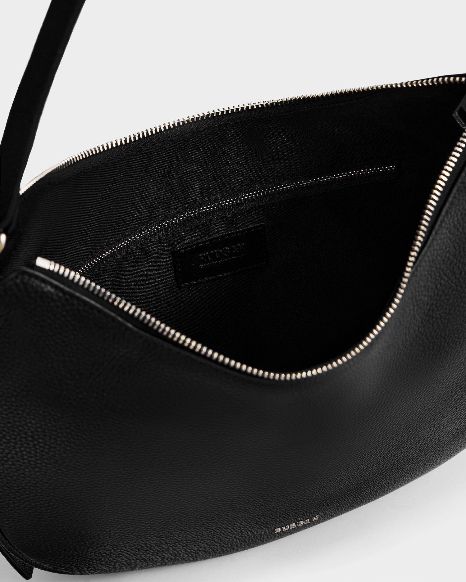 A close-up of the SYLVIA - L325515 Black by Rudsak: the women's leather shoulder bag features a zippered opening, fabric lining, and an interior pocket with a black label.
