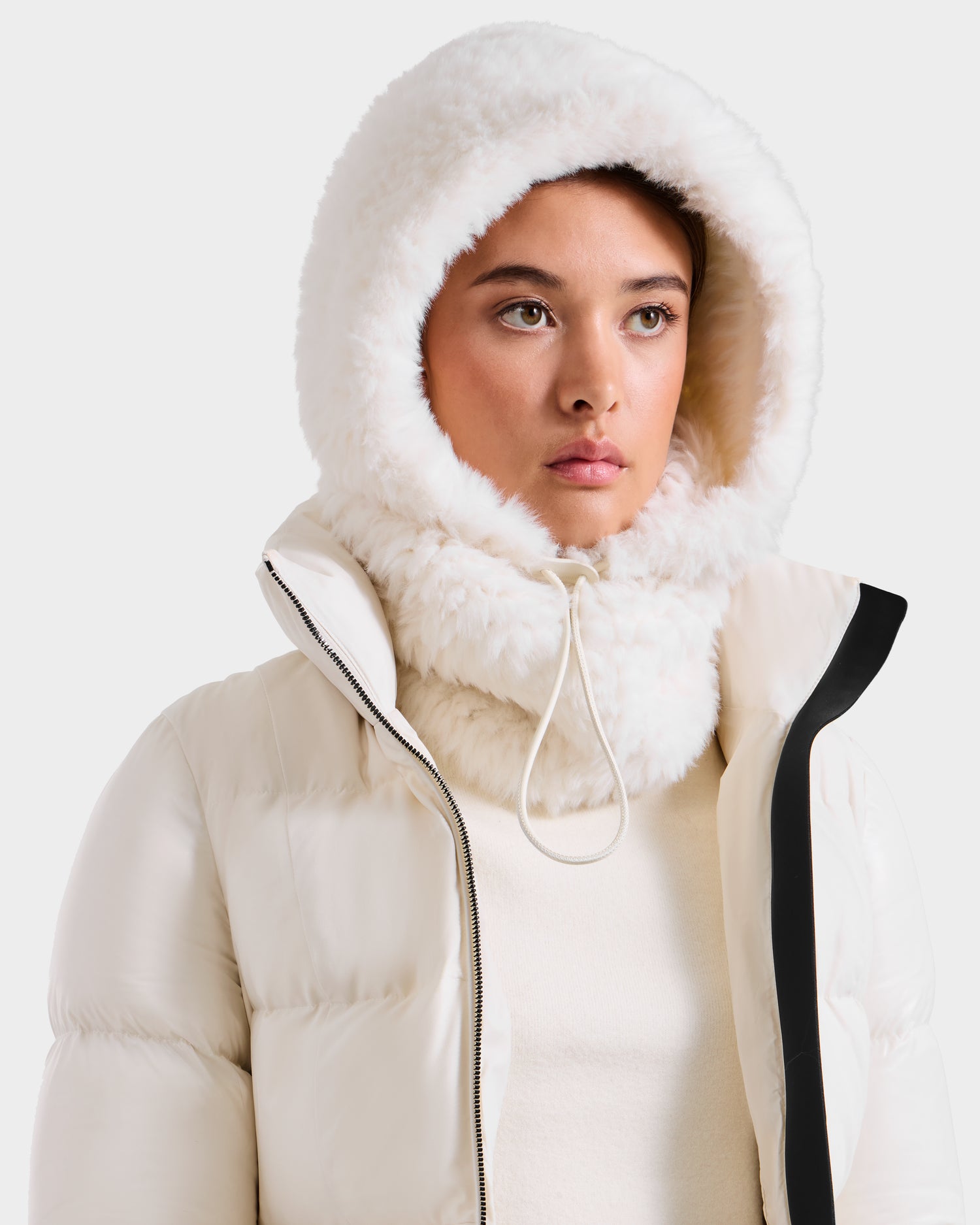 A woman models the Rudsak TARA - 8425025 Iceland white faux fur hooded jacket with high collar and drawstring, styled with a women’s balaclava, looking forward with a neutral expression against a plain background.