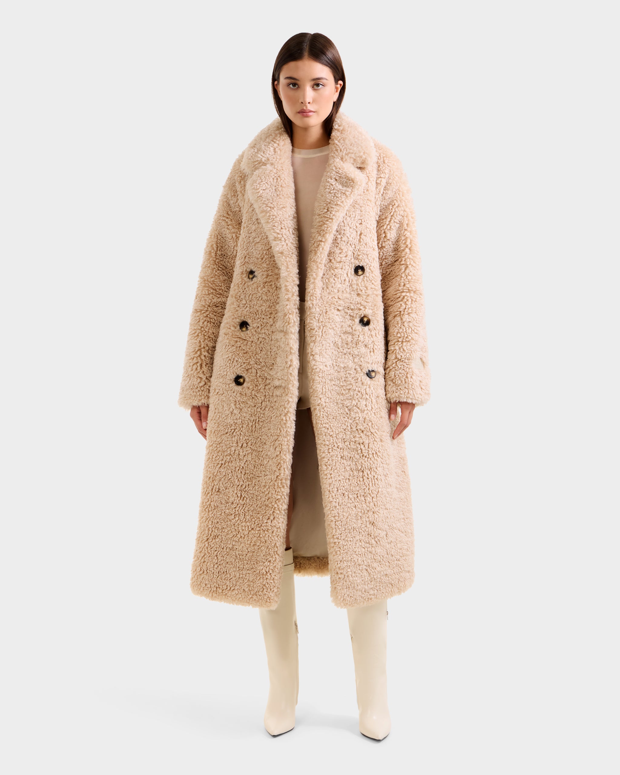 A woman faces forward wearing the Rudsak TINA - 8125968 Vanilla double-breasted teddy trench coat, paired with a matching light outfit and cream knee-high boots against a plain light background.