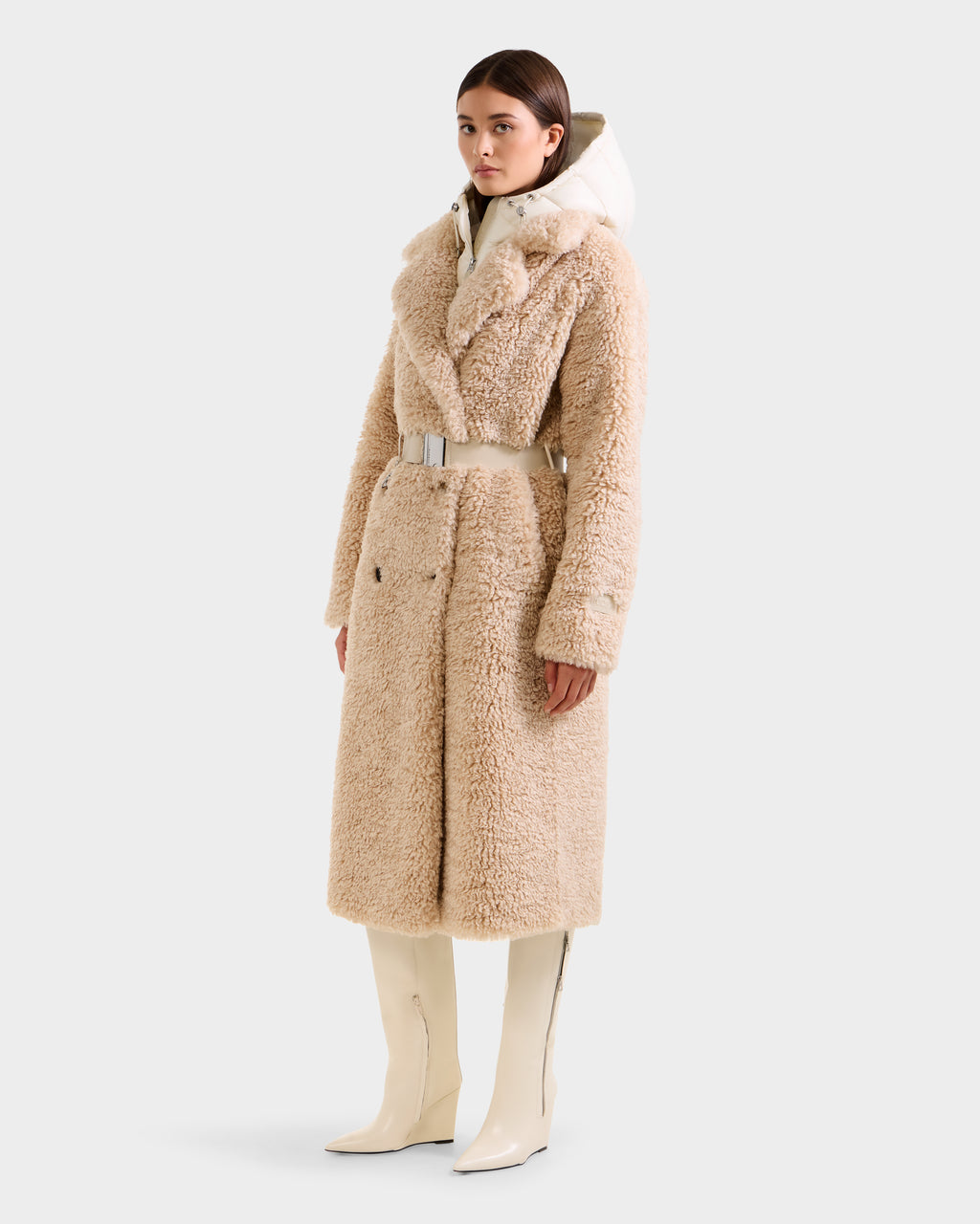 A woman wears the Rudsak TINA - 8125968 Vanilla faux fur trench coat with a wide belt, paired with a white turtleneck and knee-high white boots, standing against a plain light background.
