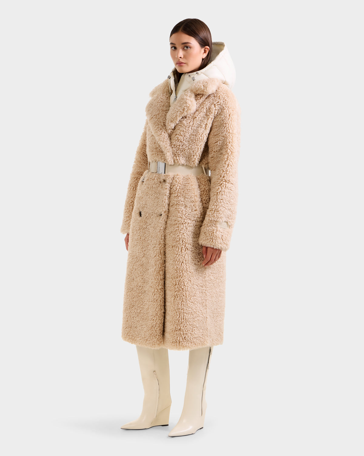 A woman wears the Rudsak TINA - 8125968 Vanilla faux fur trench coat with a wide belt, paired with a white turtleneck and knee-high white boots, standing against a plain light background.