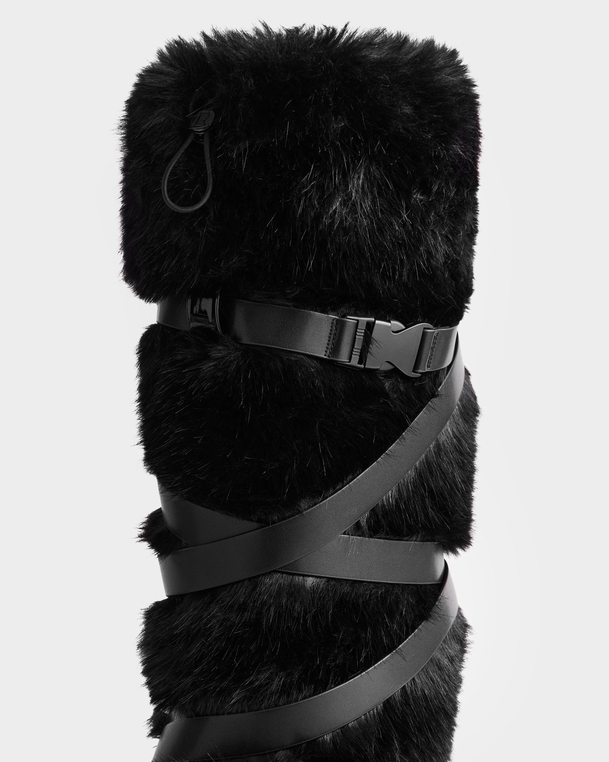 A close-up of the Rudsak TORIN - 8225029 Black women’s faux fur moon boot, featuring thick black faux fur, black straps with a plastic buckle, and a carabiner clip—a stylish winter choice—set against a plain white background.