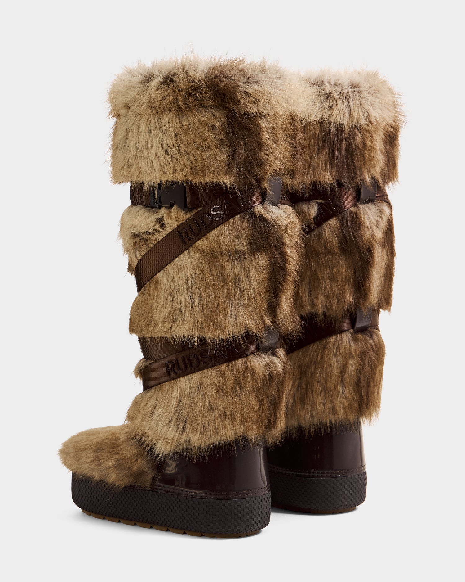 The TORIN - 8225029 Mix Mocha women's faux fur moon boots by Rudsak feature brown faux fur, black soles, and dark wrap-around straps, making them a stylish winter choice. Shown side by side on a white background.