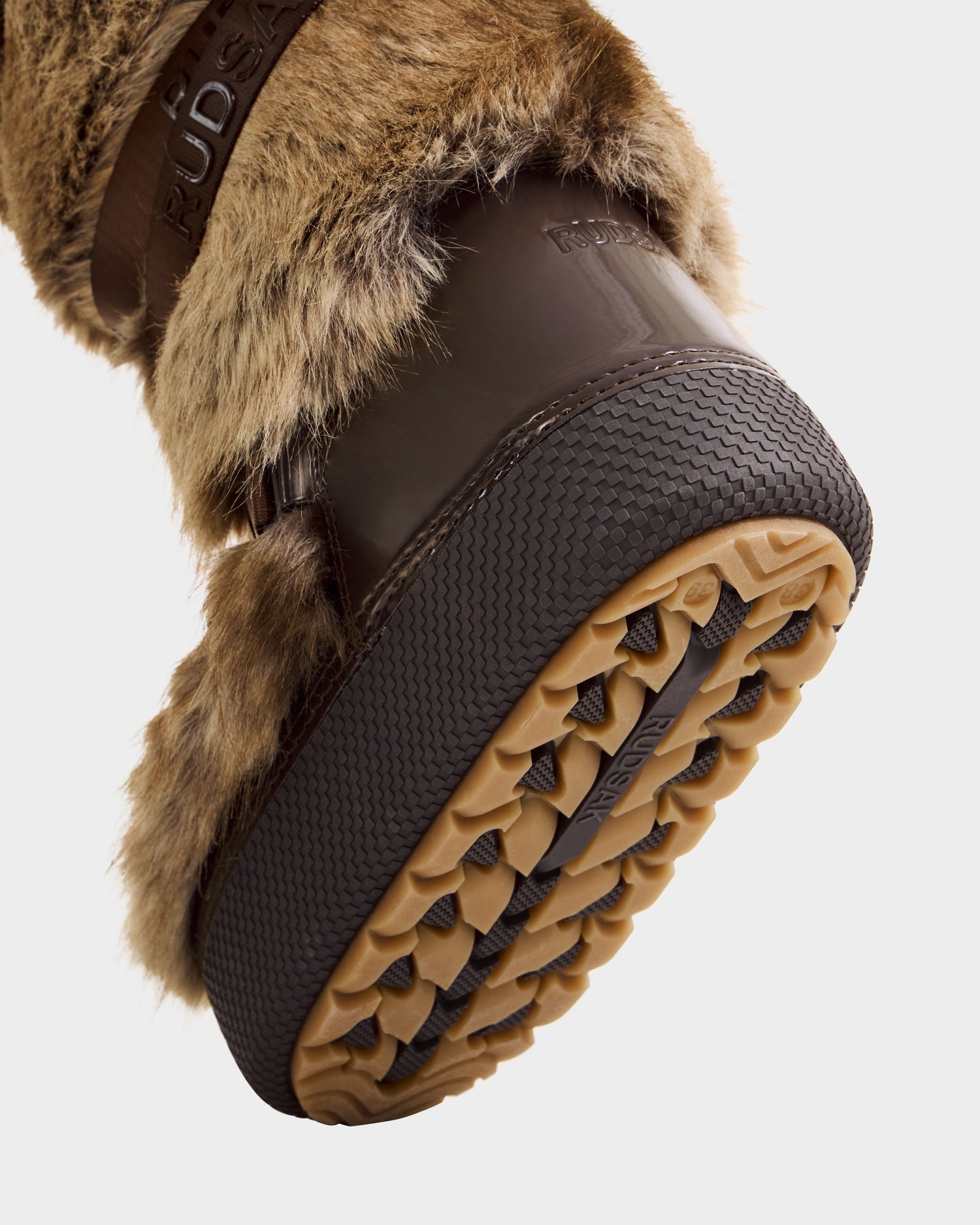 Close-up of the sole of Rudsak’s TORIN - 8225029 Mix Mocha women’s boot, showing its brown rubber tread and patterned grip, worn on foot against a plain light background.