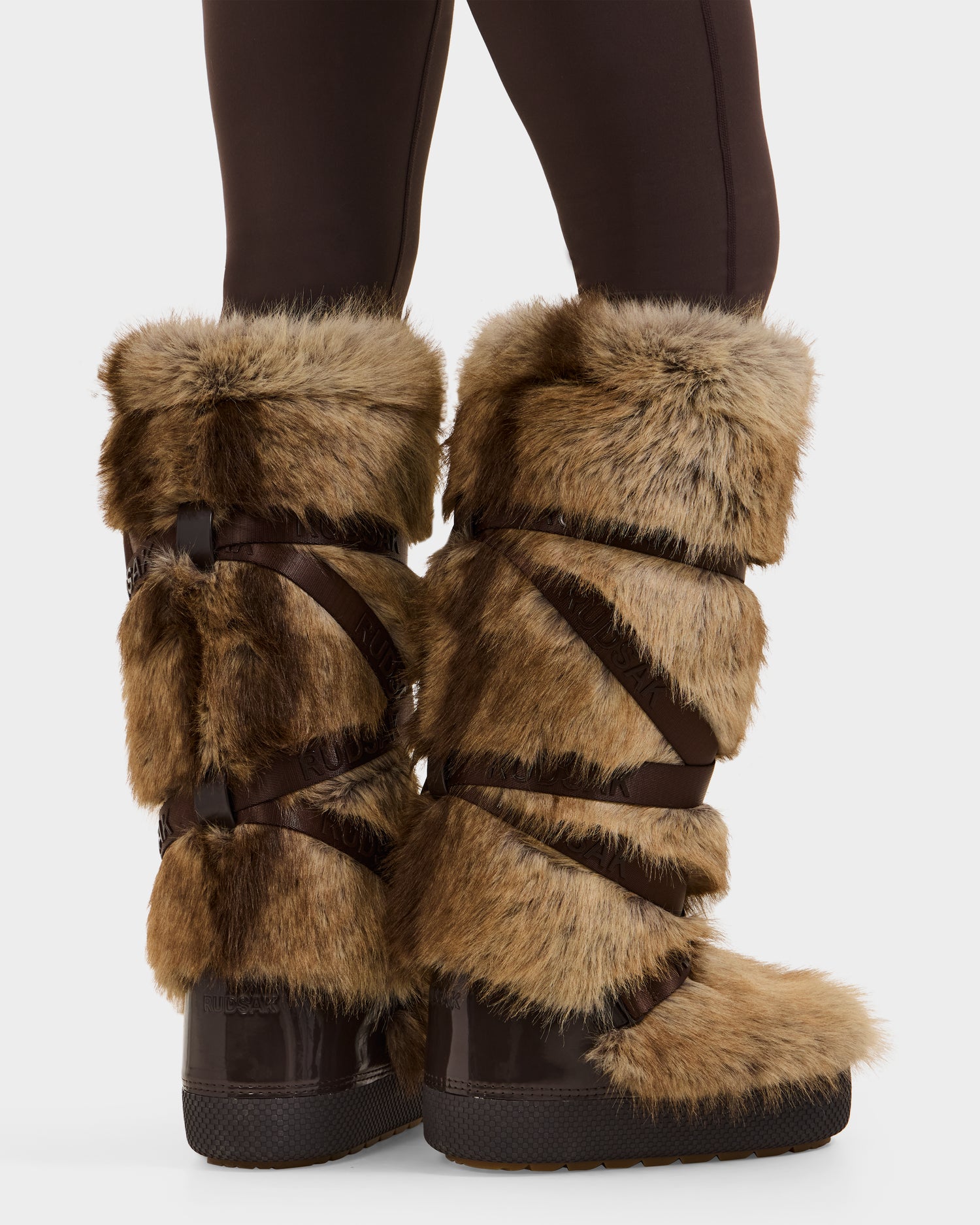 Model wearing Rudsak TORIN - 8225029 Mix Mocha tall women’s faux fur winter boots with dark brown straps, featuring a thick, plush design. Boots are styled with dark leggings and shown against a white background.