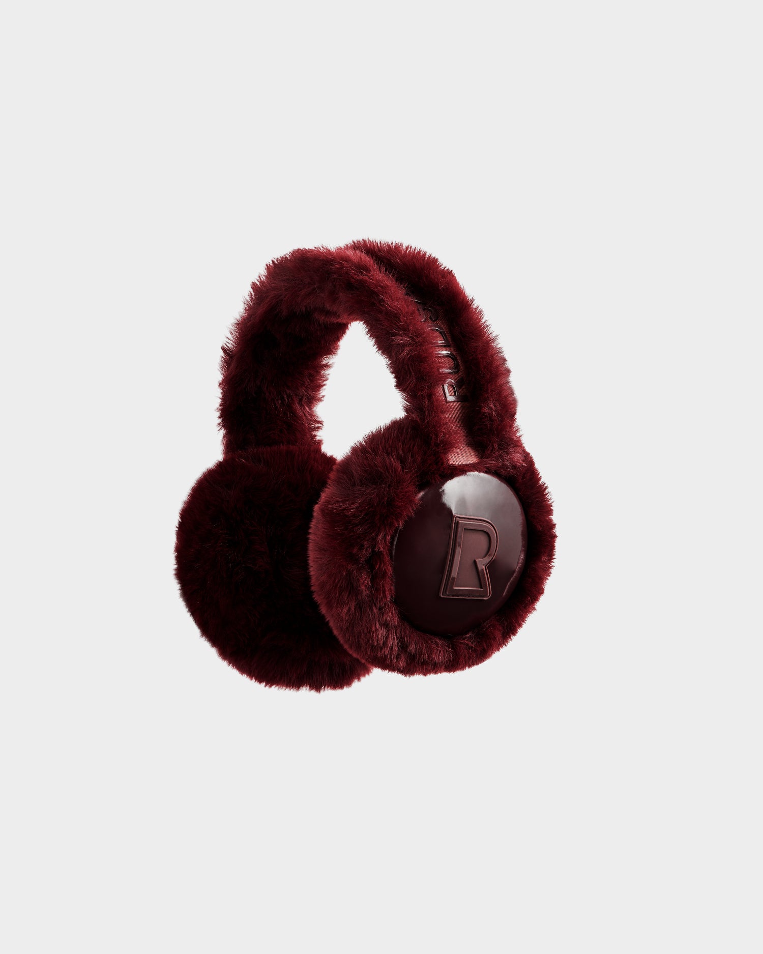 The VALENCIA - 8425543 Bordeaux earmuffs by Rudsak feature plush, dark red faux fur with a bold B logo on each ear, shown against a light grey background—a chic winter accessory for cold days.