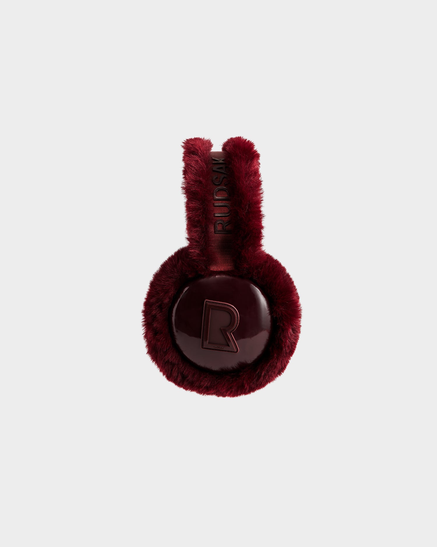 VALENCIA - 8425543 Bordeaux by Rudsak: Burgundy faux fur earmuffs with shiny, round ear covers embossed with “R” and RIUSKA text on the band—a chic winter accessory shown against a plain light background.