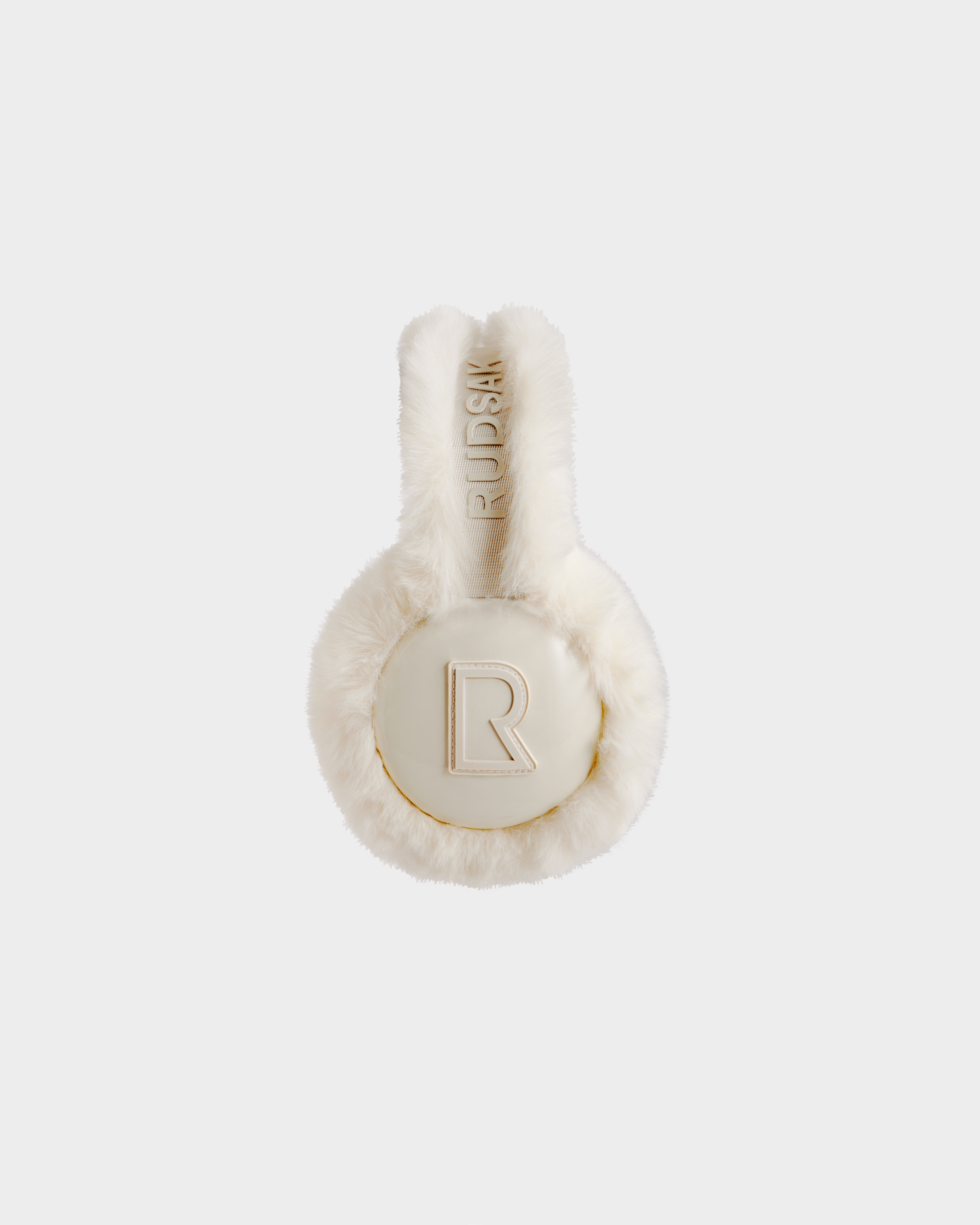 A pair of white, furry Rudsak VALENCIA - 8425543 Iceland earmuffs with round ear covers and a large gold R logo and 'RUSH' text on the headband, shown as a stylish winter accessory against a light gray background.