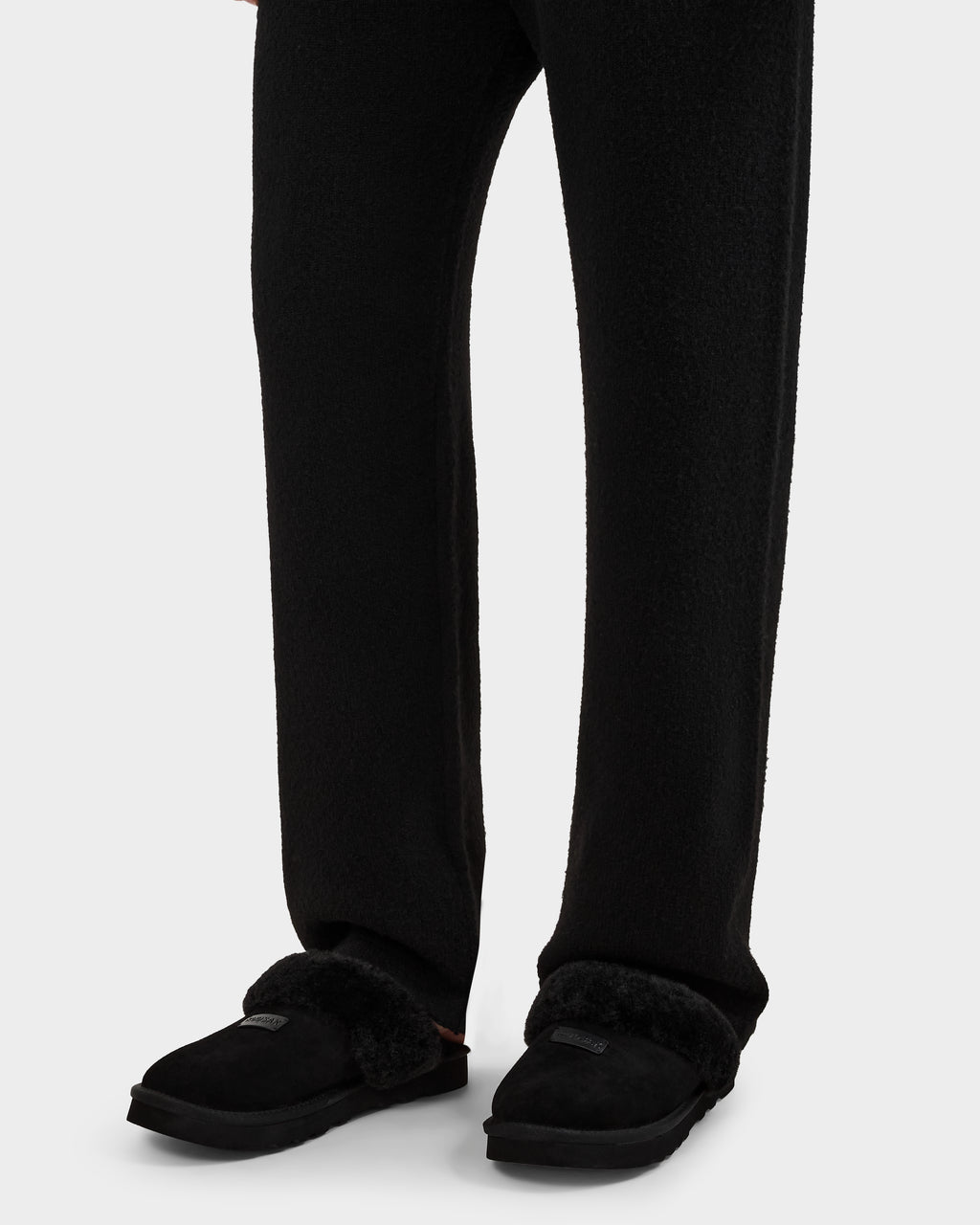 A person wearing Rudsak WILBER - 6225509 Black fleece pants and faux shearling slippers, shown from the waist down against a plain white background.