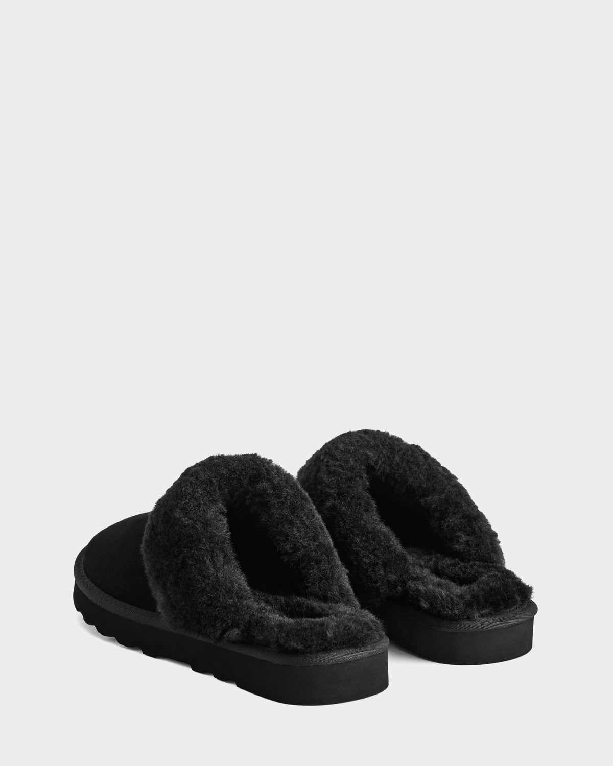 The WILBER - 6225509 Black men’s slippers by Rudsak feature thick faux shearling lining and flat soles. Shown slip-on style on a light grey background, both the back and side views are visible.