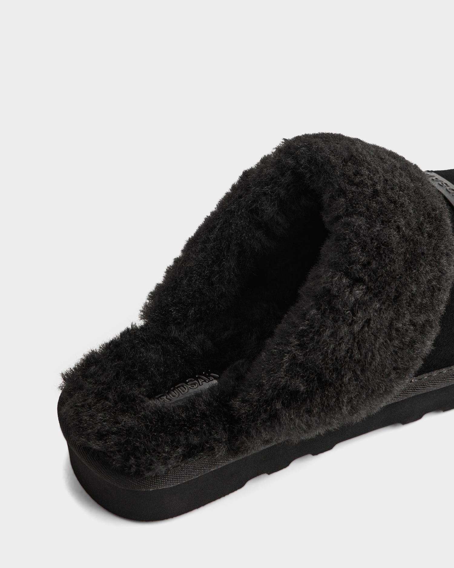 A close-up of the Rudsak WILBER - 6225509 Black men’s slipper, showcasing its suede finish, thick faux shearling lining, and textured sole, set against a white background.