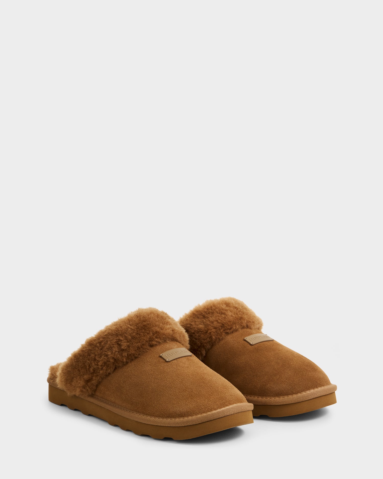 The Rudsak WILBER - 6225509 Tan men's suede slippers feature a fluffy, shearling-like lining and rubber soles, shown against a plain light gray background.