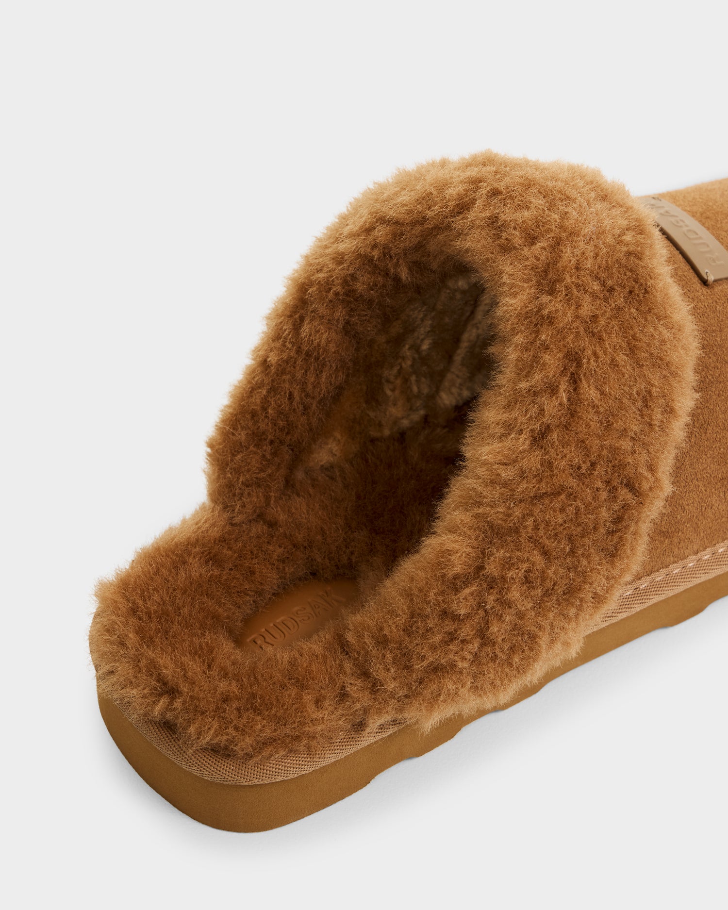 A close-up of the Rudsak WILBER - 6225509 Tan men’s slipper in brown suede, featuring a fluffy shearling-lined interior and a sturdy rubber sole, photographed against a plain white background.
