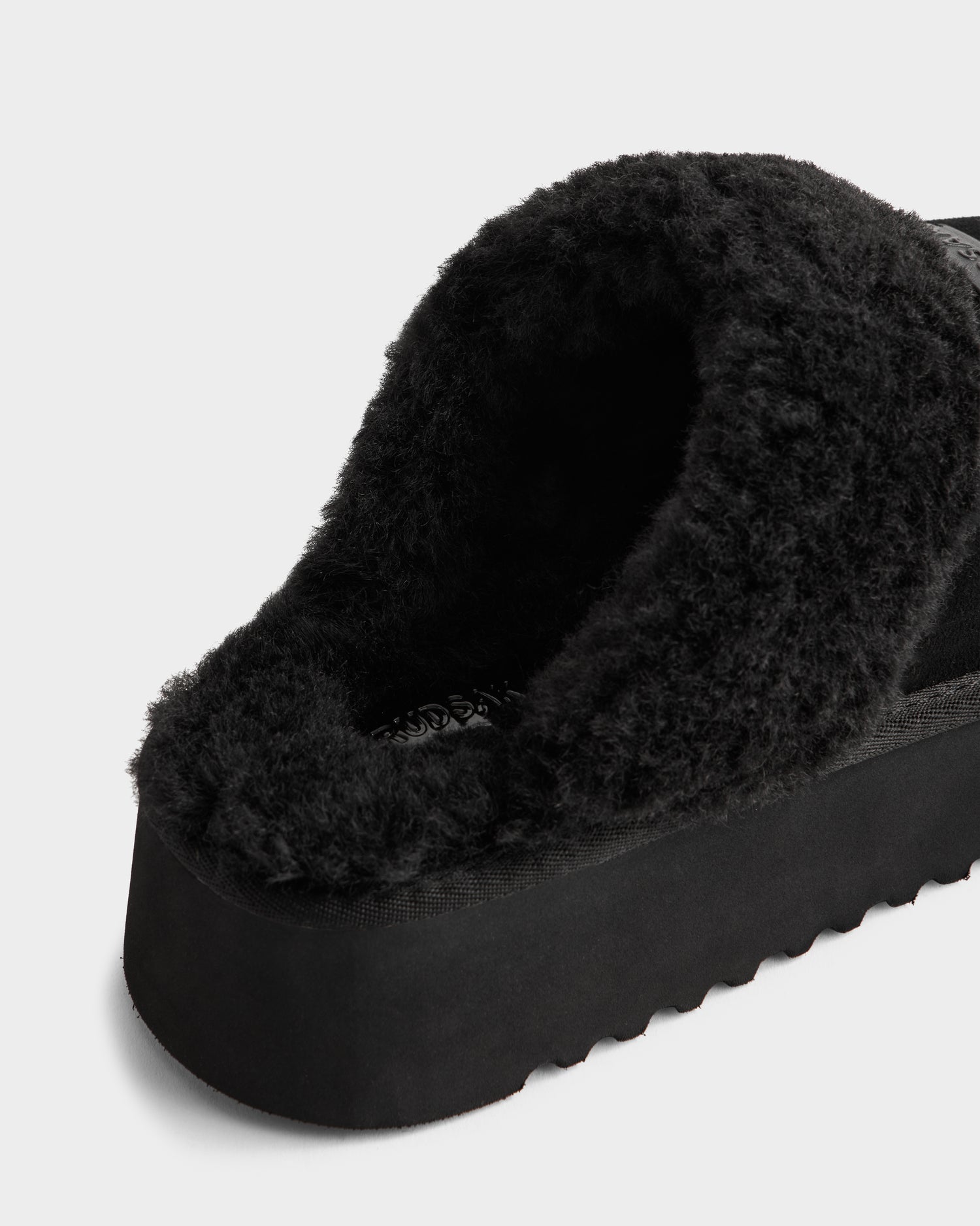 A back-angle close-up of the Rudsak WILMA - 8225582 Black women’s slipper, featuring black faux shearling and a thick sole, on a white background.