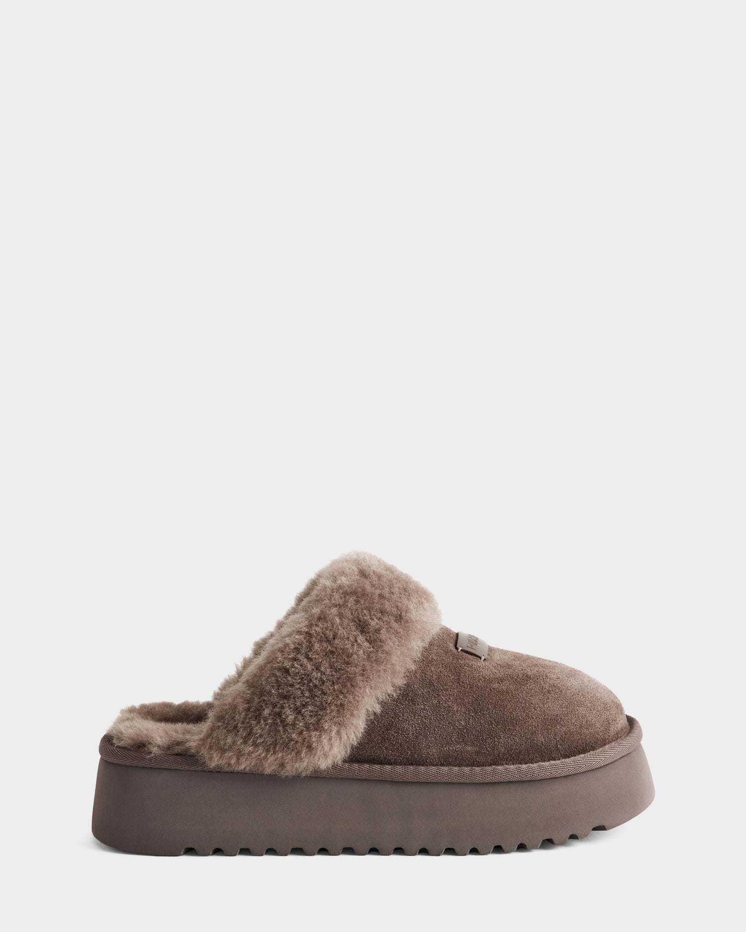 The Rudsak WILMA - 8225582 Mocha is a brown suede slipper with a thick, textured sole and plush faux shearling lining, displayed in a side view against a plain white background.
