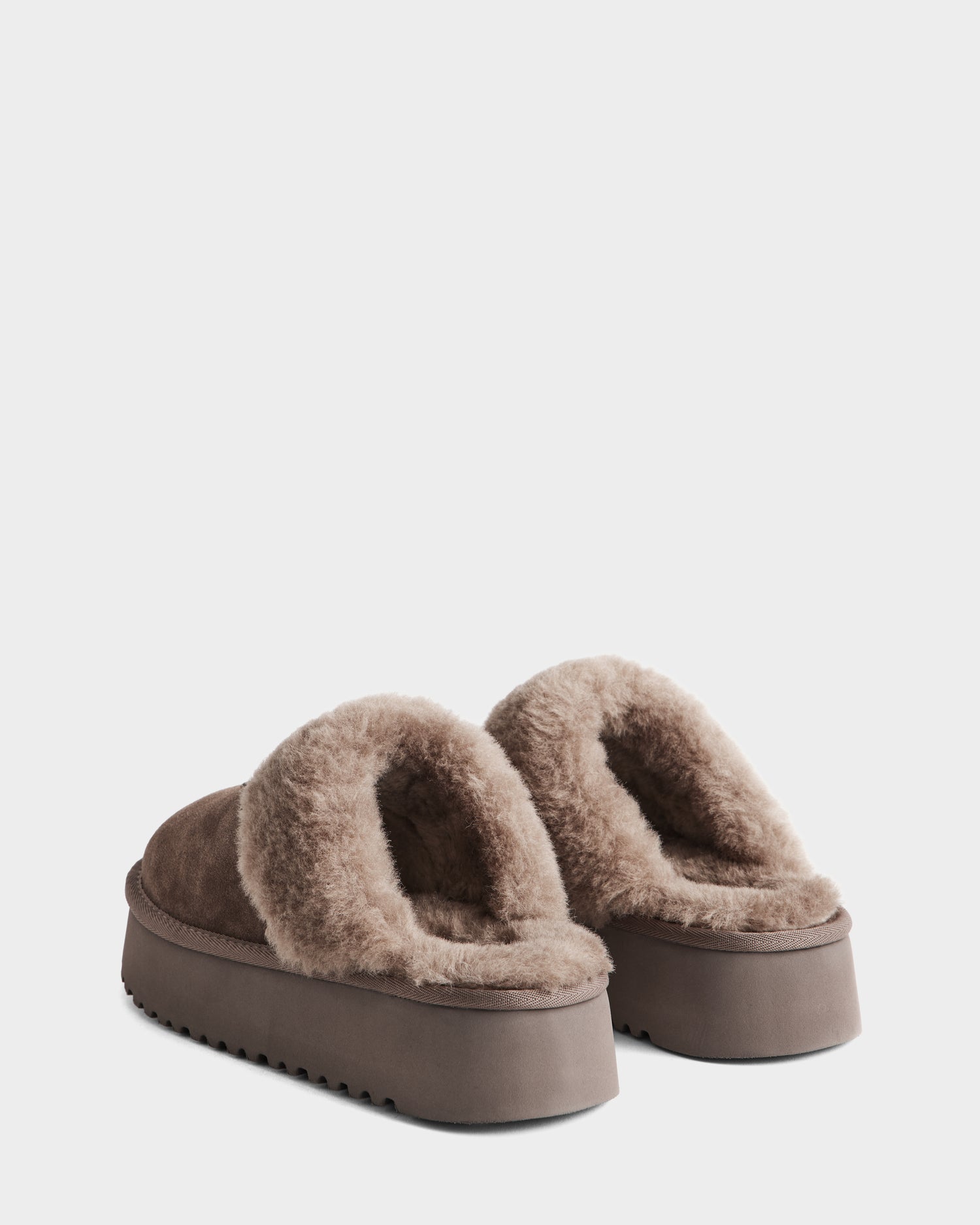 A pair of Rudsak WILMA - 8225582 Mocha women’s suede slippers featuring thick faux shearling linings and chunky rubber soles, displayed side by side on a plain white background.