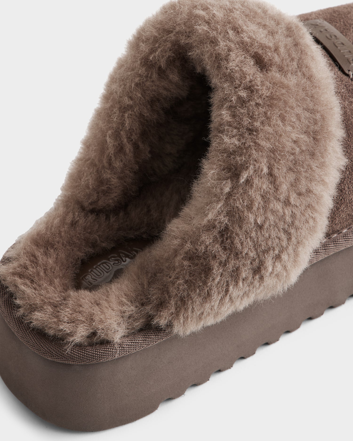A close-up of the Rudsak WILMA - 8225582 Mocha women’s slipper in soft suede with thick faux shearling lining and a textured sole, photographed on a plain white background.