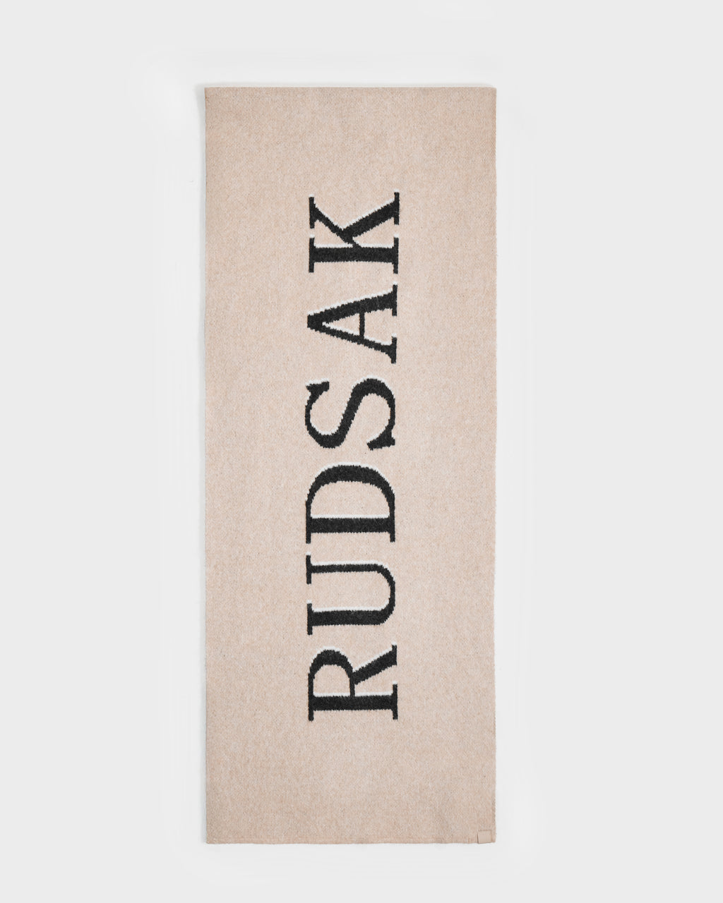 The Rudsak WYATT - 6425039 Vanilla is a beige rectangular men’s scarf with “RUDSAK” in bold black letters vertically, making it a stylish cold-weather essential for winter.