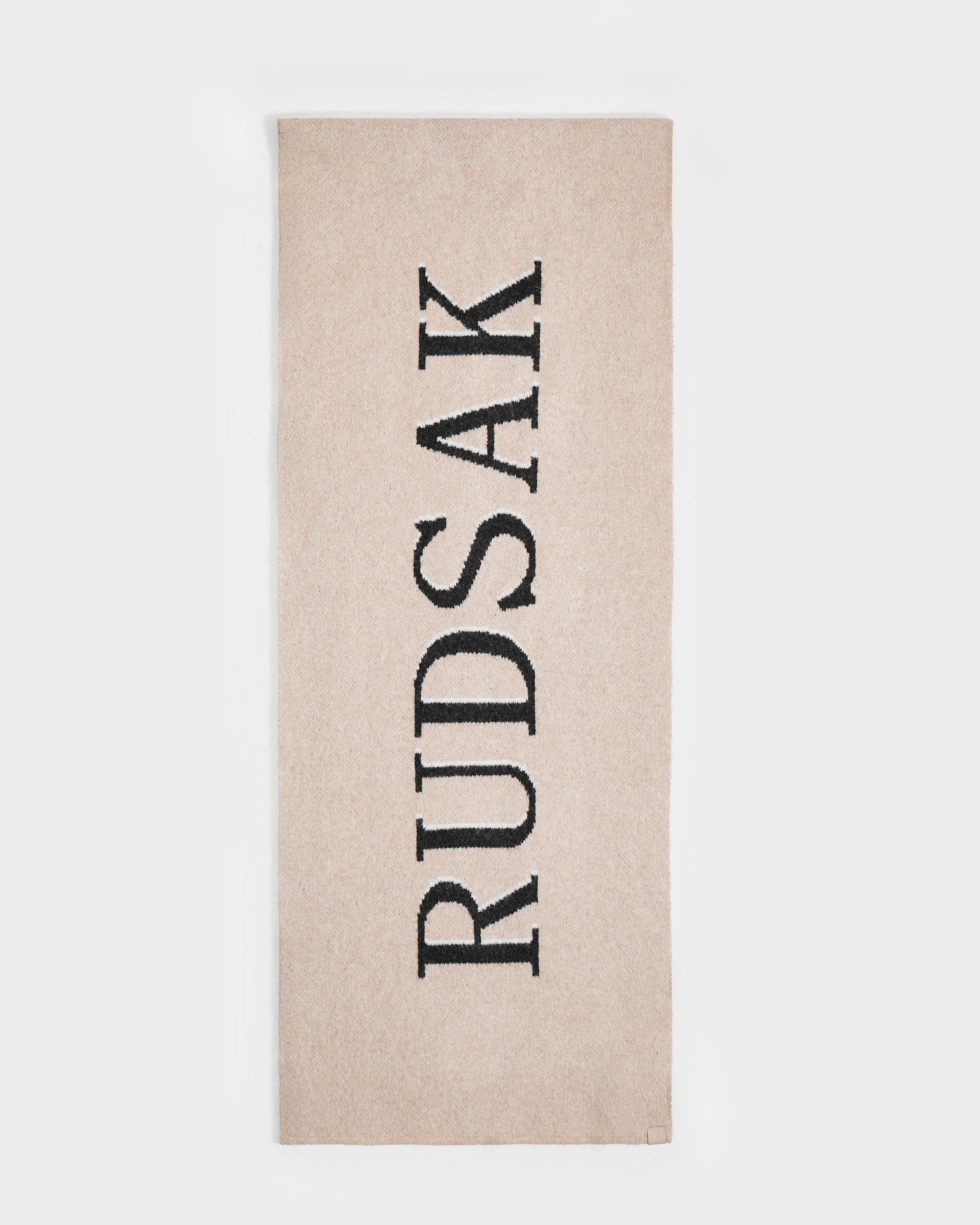 The Rudsak WYATT - 6425039 Vanilla is a beige rectangular men’s scarf with “RUDSAK” in bold black letters vertically, making it a stylish cold-weather essential for winter.