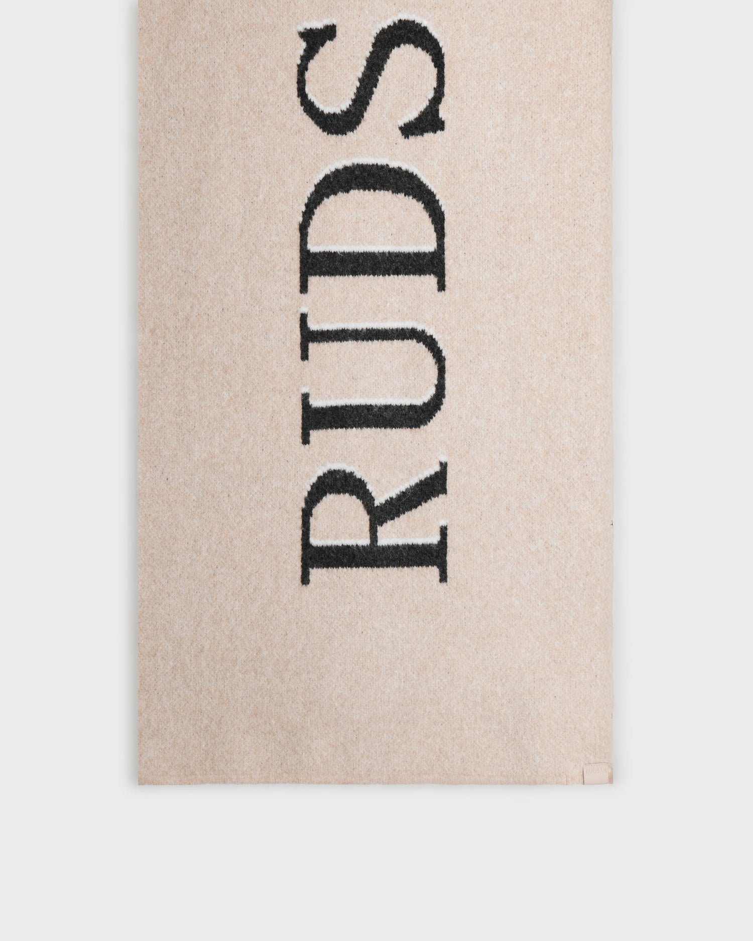 The WYATT - 6425039 Vanilla rug by Rudsak is a beige rectangular rug, inspired by winter style, featuring large black vertical "RUDS" lettering—making it a cozy cold-weather essential for any room.