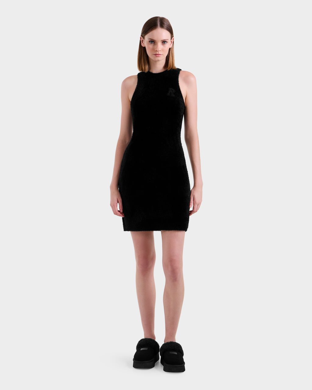 A woman faces forward in a Rudsak ZARAH - 8525696 Black fitted dress and black platform shoes, against a plain light gray background.