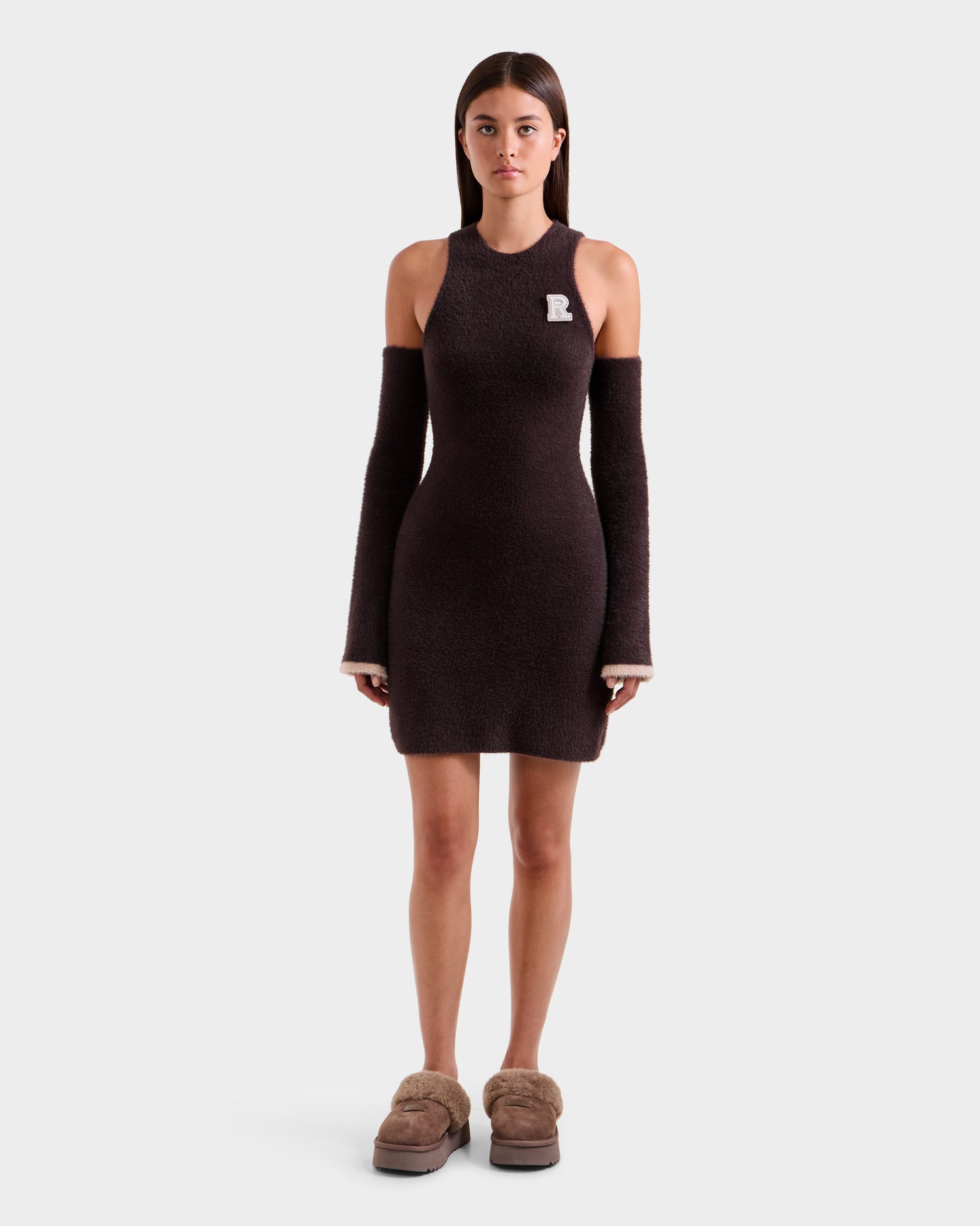 A woman faces forward in the Rudsak ZARAH - 8525696 Espresso women's fitted fuzzy knit dress with detached long sleeves, tan slip-ons, and a pin on her left chest, standing against a plain white background in an après-ski look.