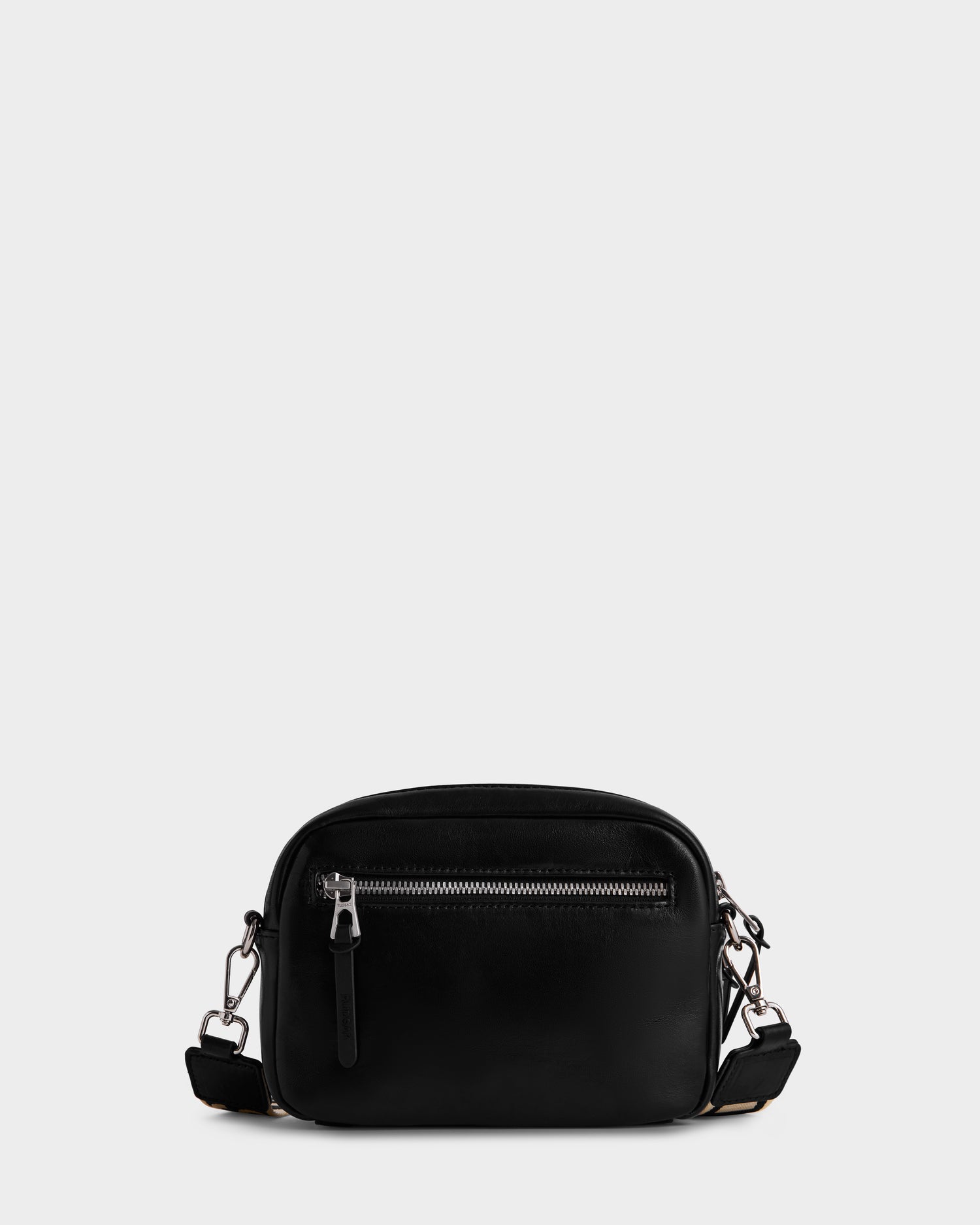 The Rudsak ZOYA L - 8325543 Black is a small black crossbody bag in smooth leather, with a front zip pocket, silver hardware, and an adjustable strap, shown on a plain light gray background.