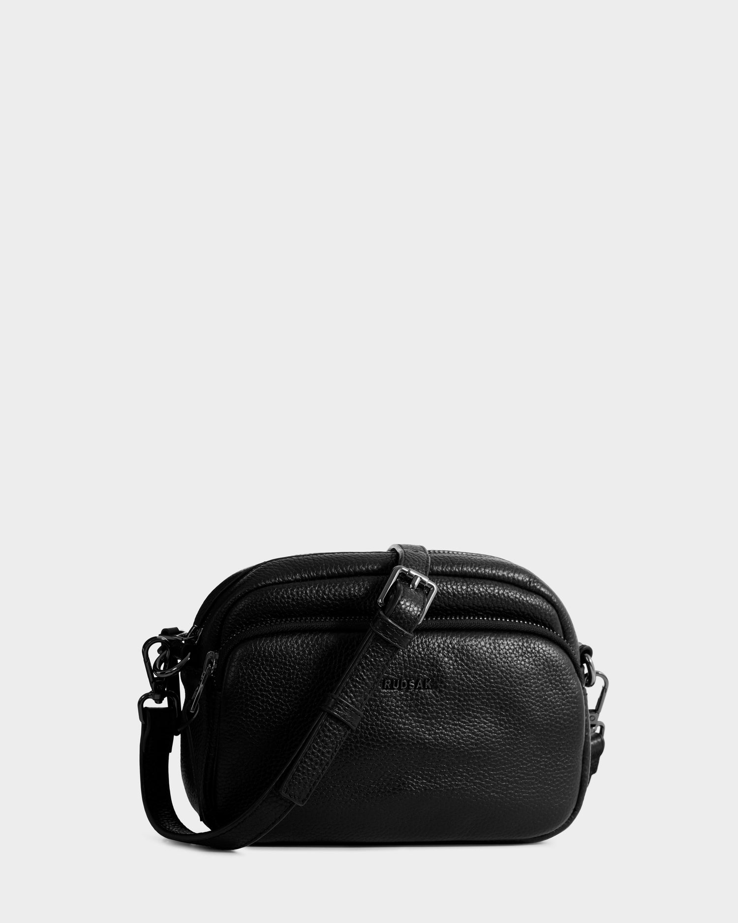The Rudsak ZOYA - L325015 Black women’s crossbody bag showcases pebbled leather, double zippered compartments, and an adjustable strap, all set against a plain light background.