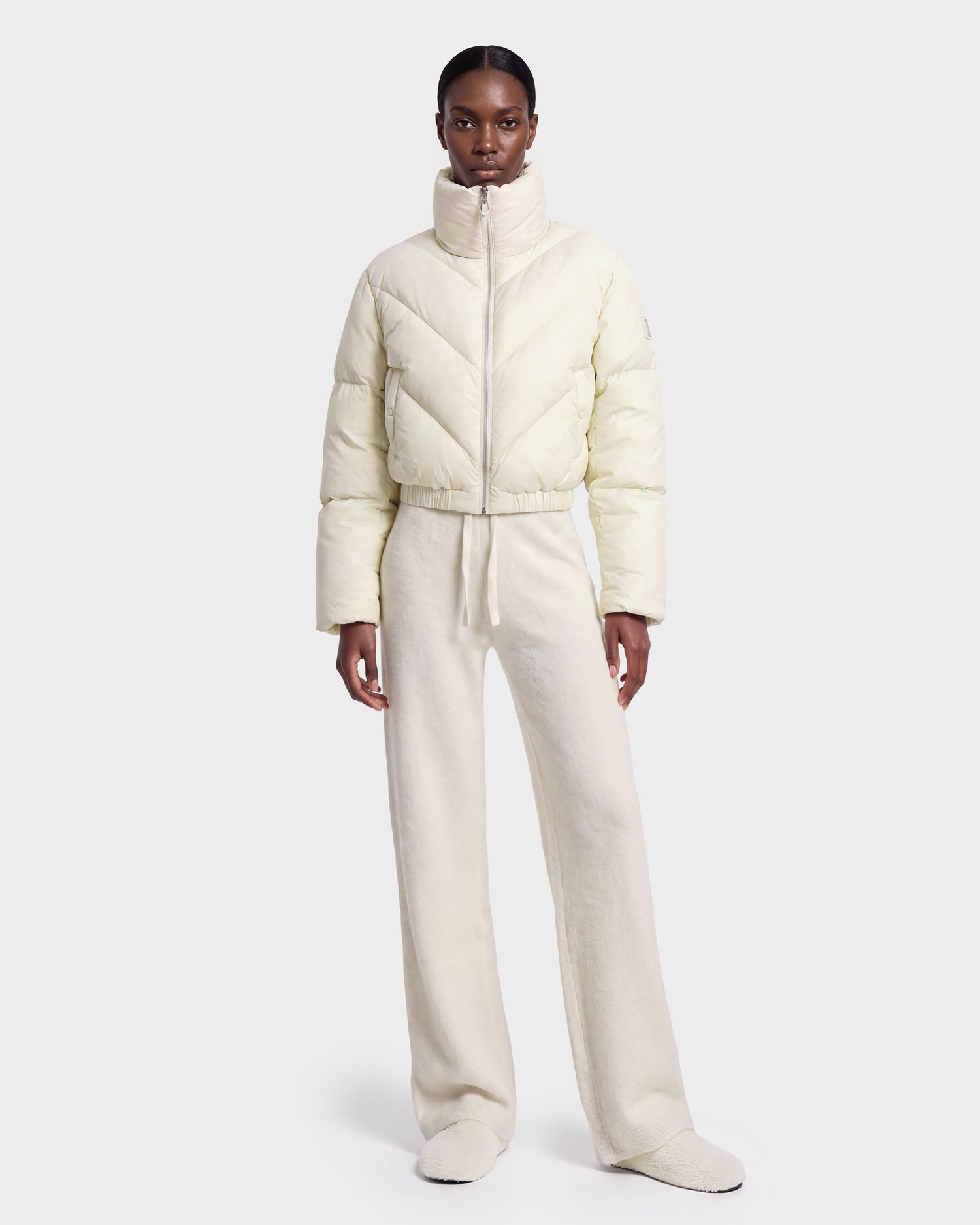 A woman stands facing forward against a plain white background, wearing the Rudsak ANSLIE - 8126986 Vanilla cropped puffer jacket and matching wide-leg pants.
