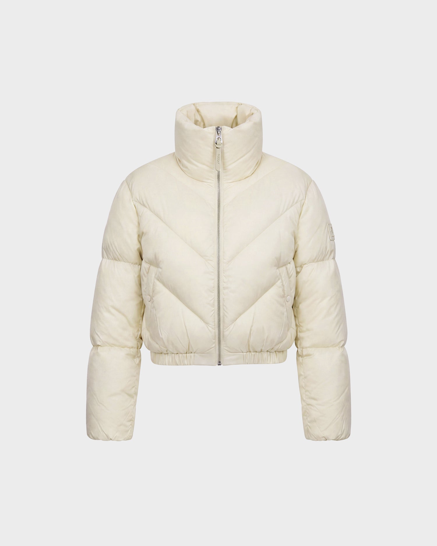 The ANSLIE - 8126986 Vanilla by Rudsak is a cream-colored women’s cropped puffer jacket, featuring a high collar, front zipper, and long sleeves. Crafted with RDS-certified down, this stylish piece is showcased against a plain white background.