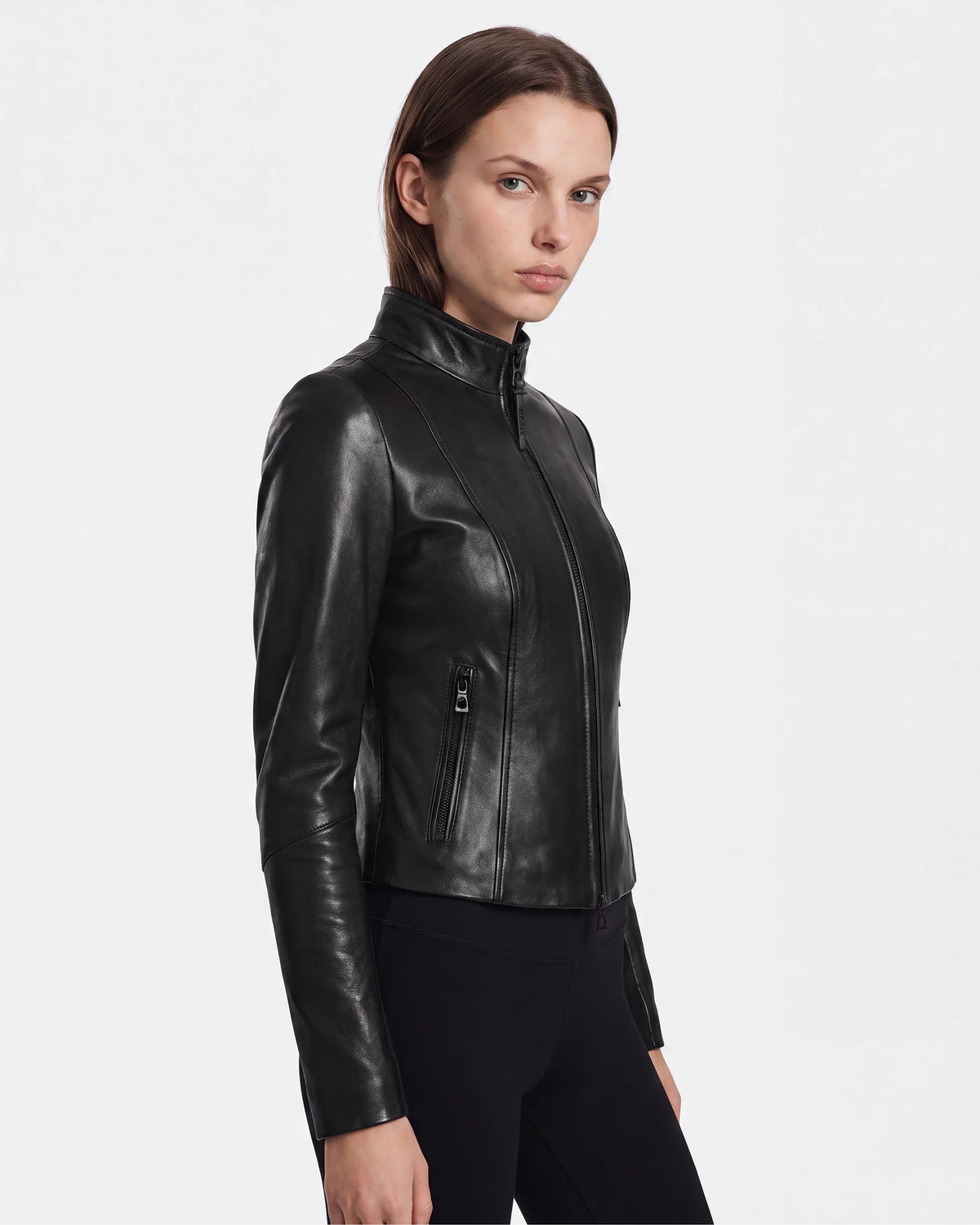A woman wearing the ABIGAIL - 8124560 Black leather jacket by Rudsak and black pants stands against a plain white background, looking slightly to the side with a neutral expression.
