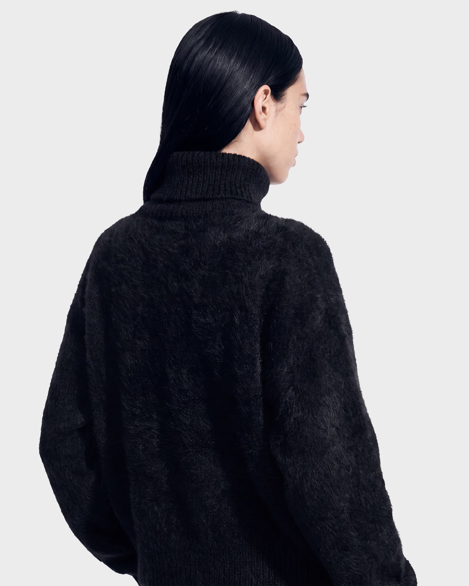 A person with long dark hair, seen from behind against a plain light gray background, is wearing the Rudsak ALISYA - 8526505 Black fuzzy turtleneck sweater.