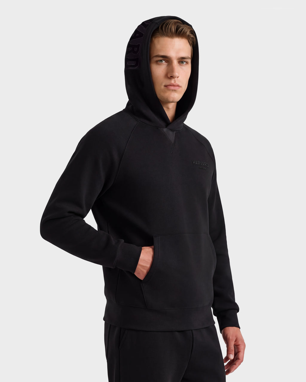 A young man wearing the Rudsak BARRY HV - H525500 Black hoodie stands against a plain light background with one hand in his pocket, looking confidently at the camera.