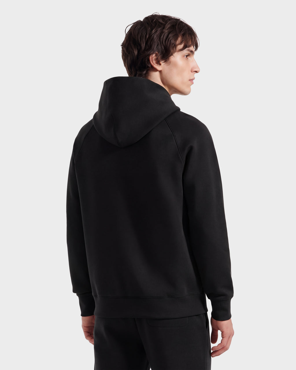 A person with short brown hair, dressed in the limited-edition Rudsak BRIAR R HV - H525506 Black hoodie and black pants, is standing and facing away from the camera against a plain light background.