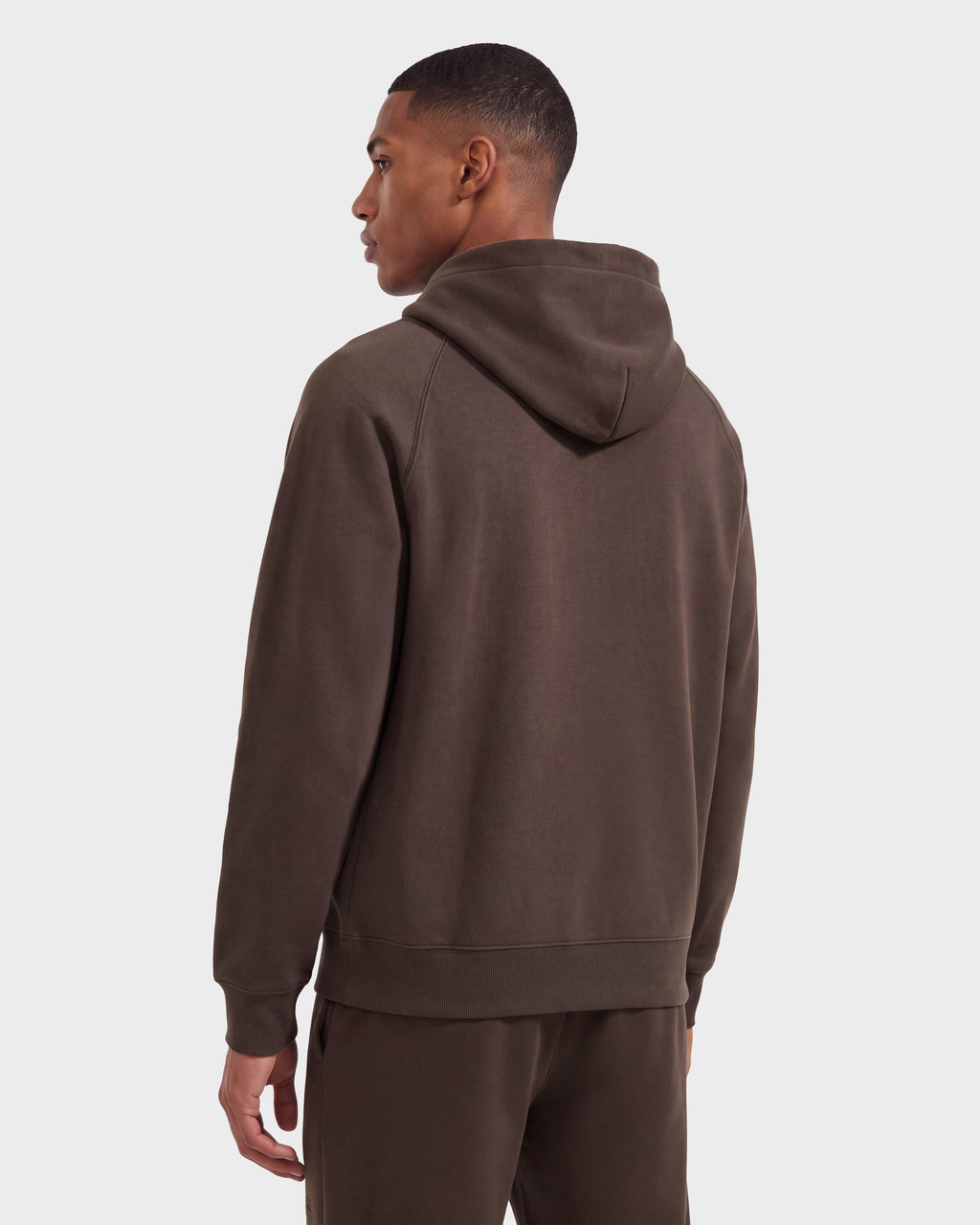 A man stands facing away, wearing a limited-edition Rudsak BRIAR R HV - H525506 hoodie and matching pants in Espresso against a plain white background.