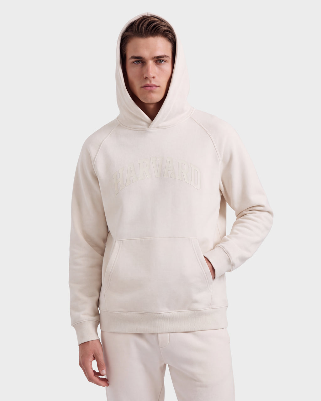 A young man wearing a light beige Rudsak BRIAR R HV - H525506 Vanilla hoodie stands against a plain white background, with one hand in his pocket and the hood up.