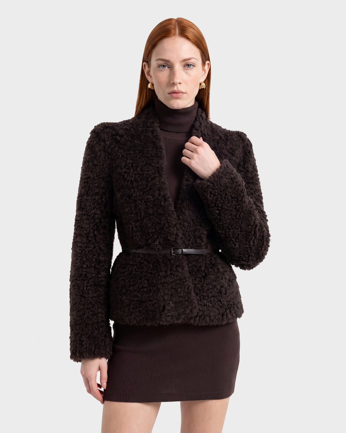 A woman with straight red hair wears the Rudsak BRINLEY - 8126980 Espresso textured jacket over a matching belted dress, standing against a plain white background.