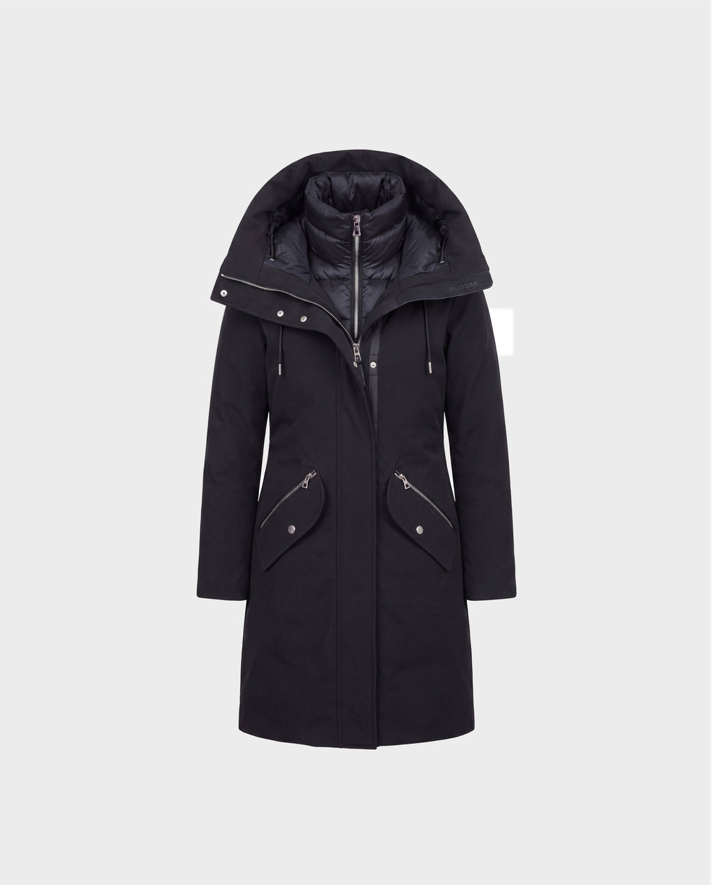 The Rudsak BRITTANY - 8125966 Black is a long black winter coat designed as premium outerwear, showcasing a wide, padded collar, zippered front closure, and two angled zip pockets with flaps. The coat is displayed on a plain light gray background.