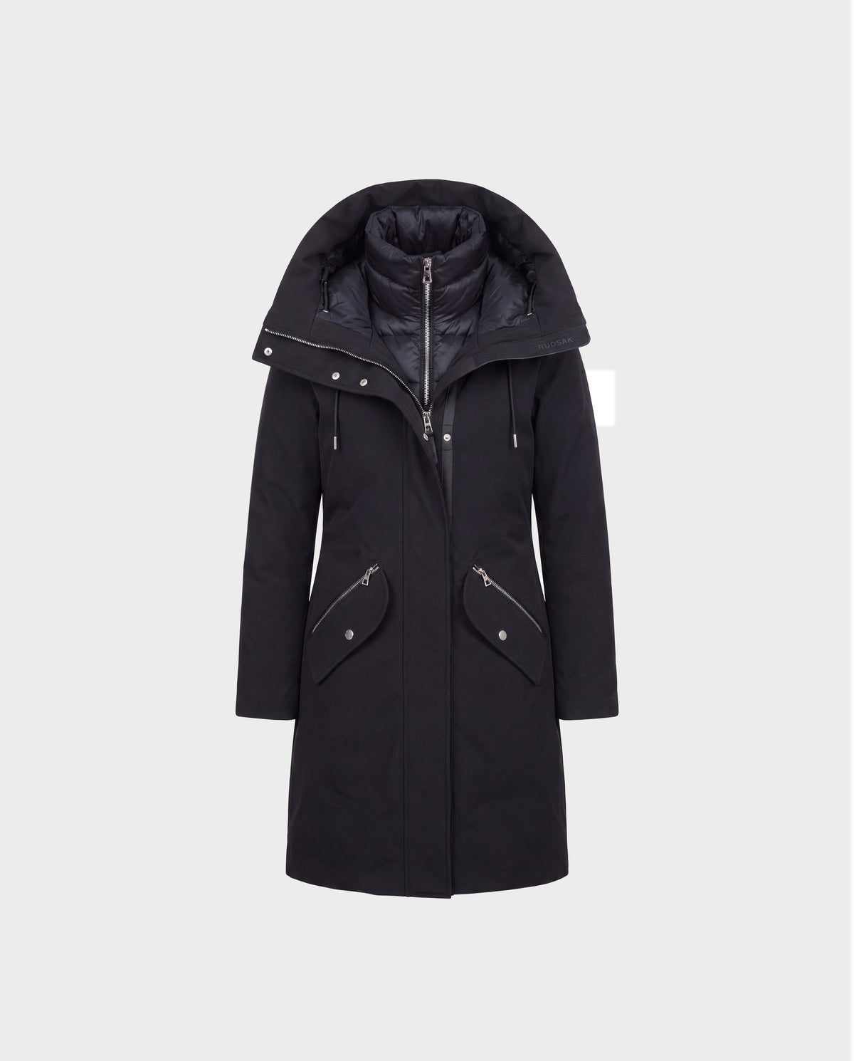 The Rudsak BRITTANY - 8125966 Black is a long black winter coat designed as premium outerwear, showcasing a wide, padded collar, zippered front closure, and two angled zip pockets with flaps. The coat is displayed on a plain light gray background.