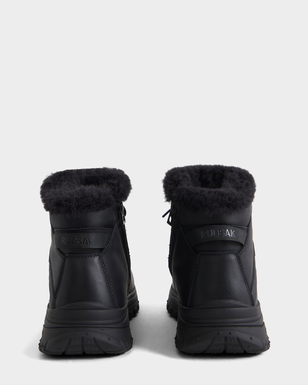 A pair of BRYSON - 6226504 Black winter boots with fur trim and lugged outsole, seen from the back on a white background. The Rudsak logo appears on the heel of each boot.