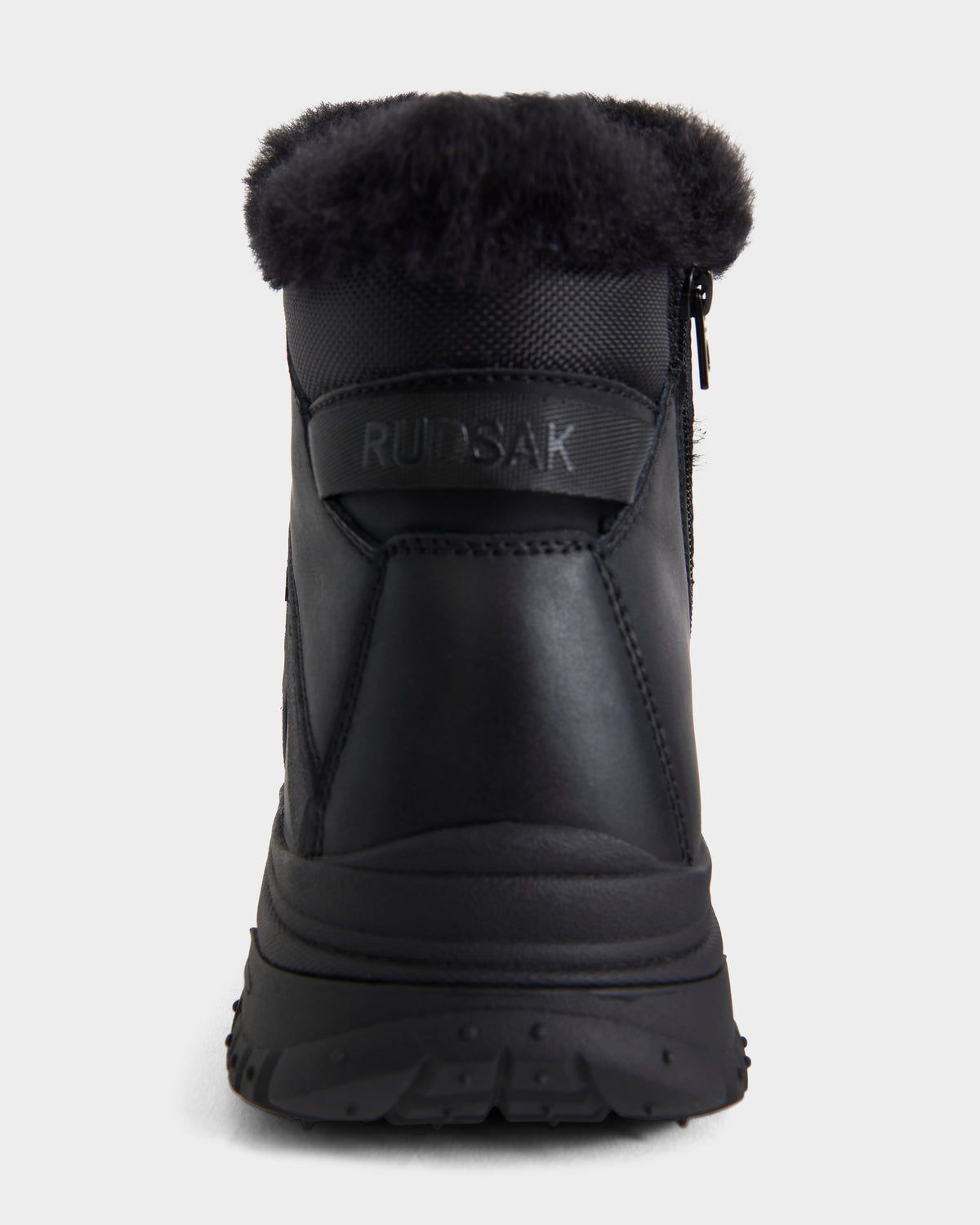 The BRYSON - 6226504 Black winter boot by Rudsak is shown from the back, featuring a fur collar, lace-up design, side zipper, and RUDSAK embossed on a leather patch above the heel.