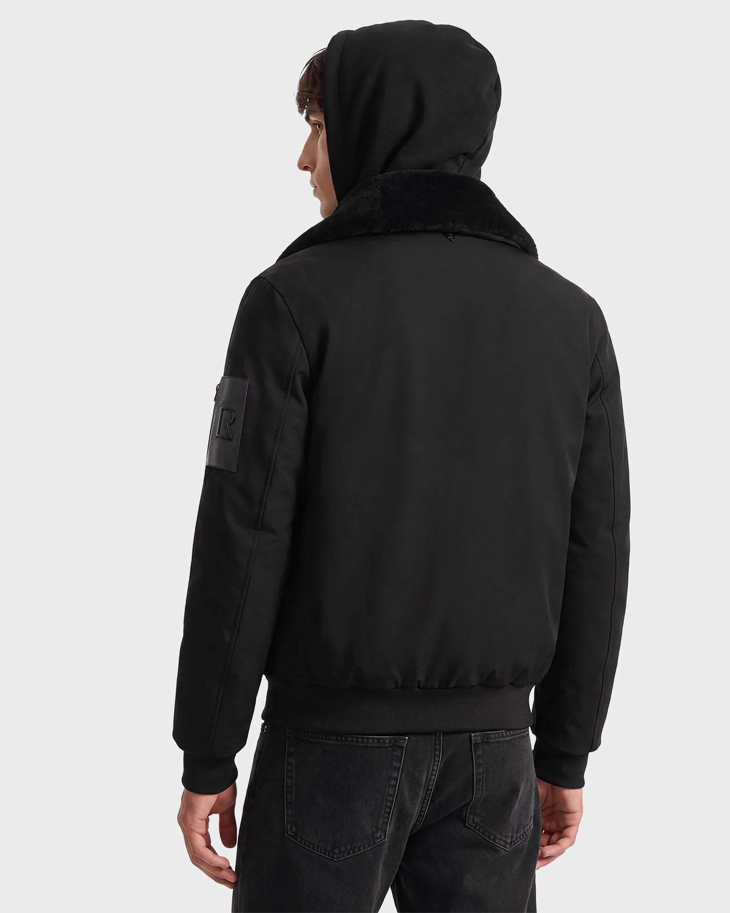 A person wearing the Rudsak DYLAN - 6125593 Black men’s aviator bomber jacket with a faux fur collar and black jeans, shown from the back looking over their left shoulder against a plain background.